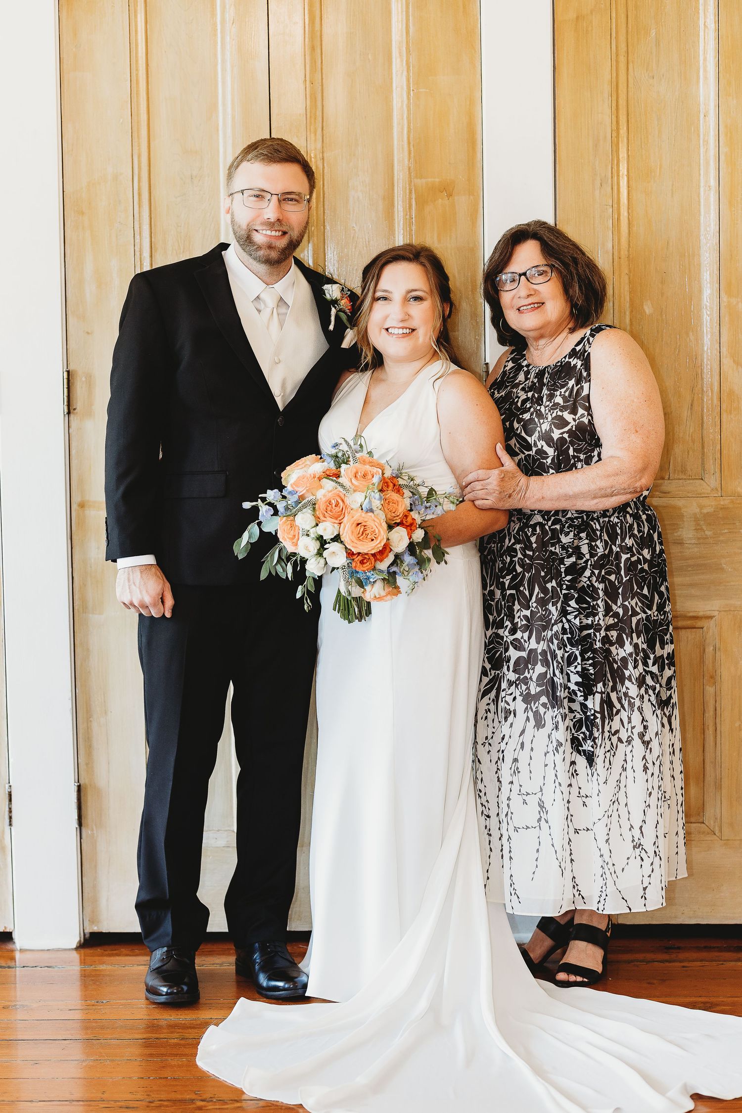 Wedding group photo with bride in white dress and guest in patterned black dress.