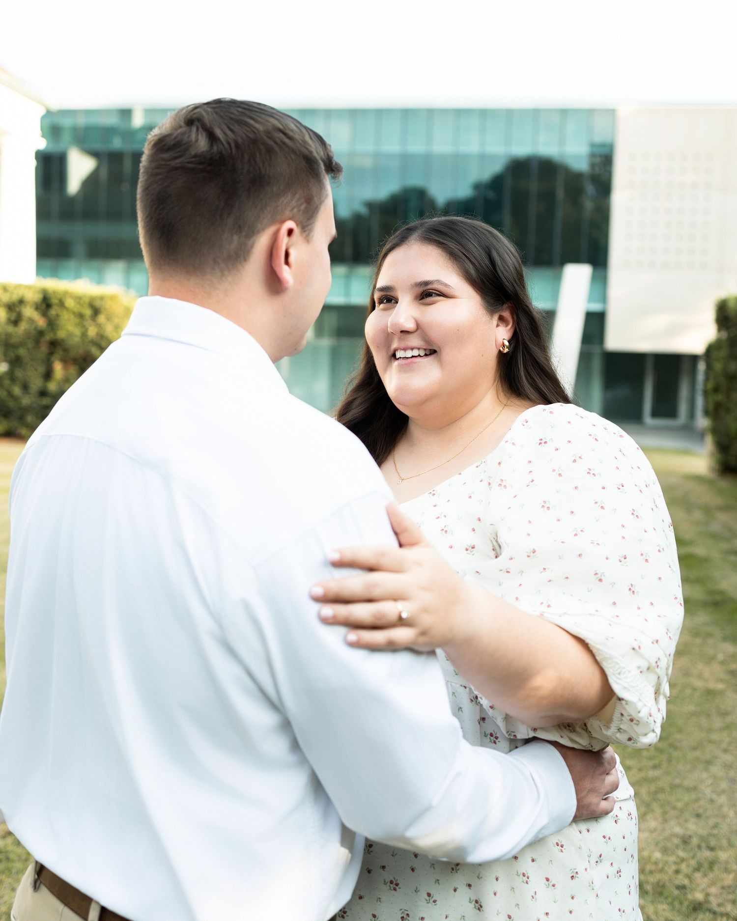 A couple in formal attire share a romantic dance outdoors near a modern building.