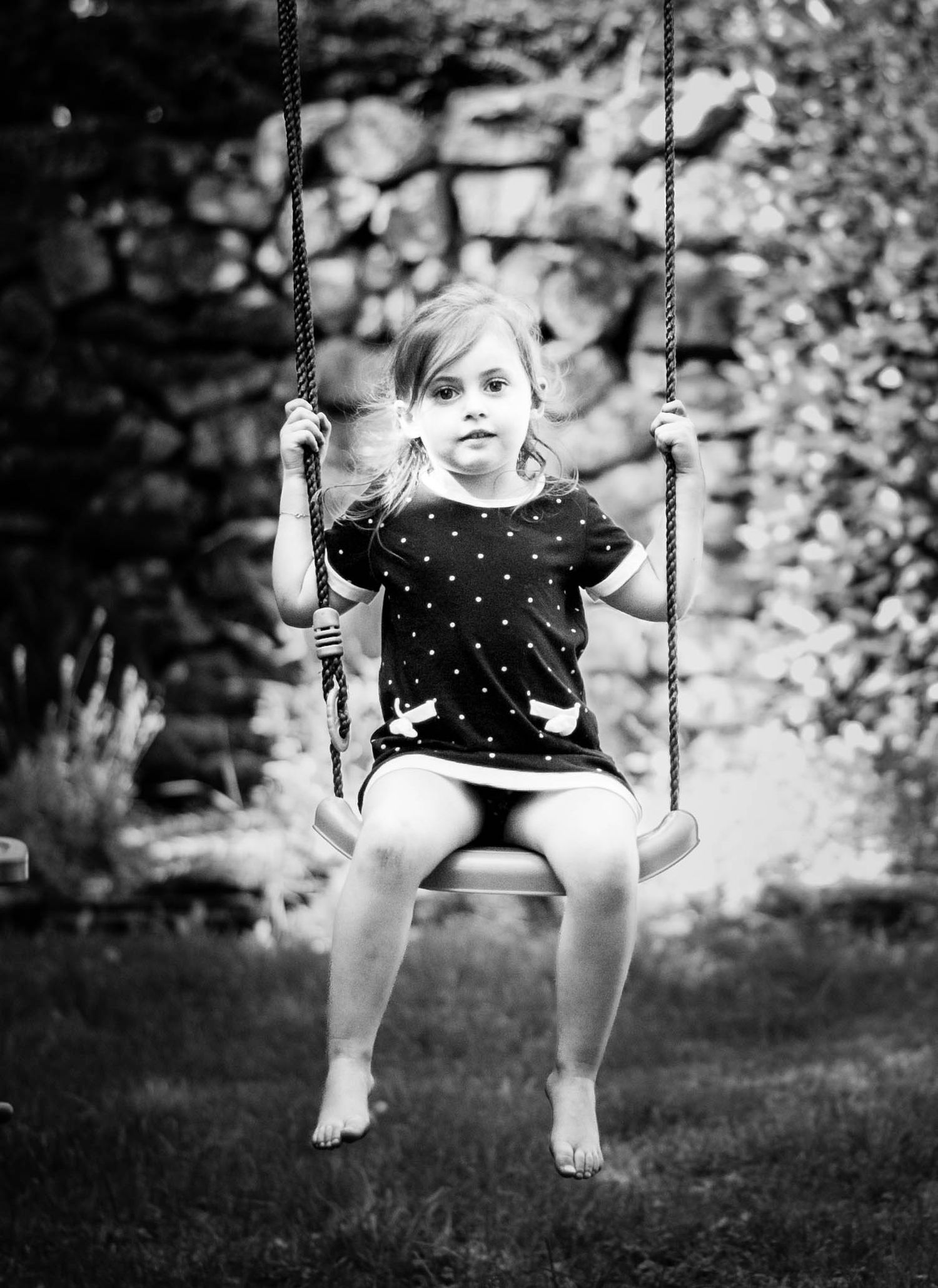 Portrait en noir et blanc d’une enfant sur une balançoire, capturé avec intimité et douceur. Photographe de famille, Ouest lyonnais.