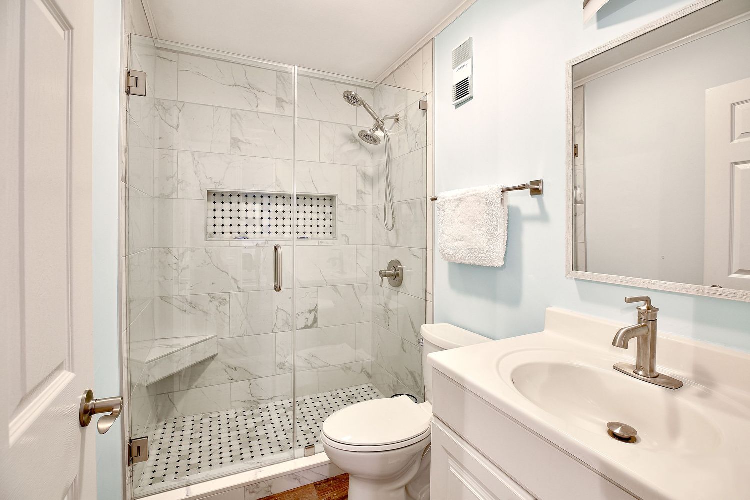 Modern white bathroom with marble-tiled walk-in shower, mosaic floor tiles, toilet, and single vanity with sink.