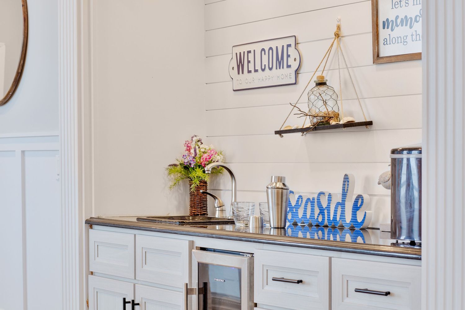 Coastal welcome bar area with shiplap walls, open shelving, wine fridge, and seaside decor accents.