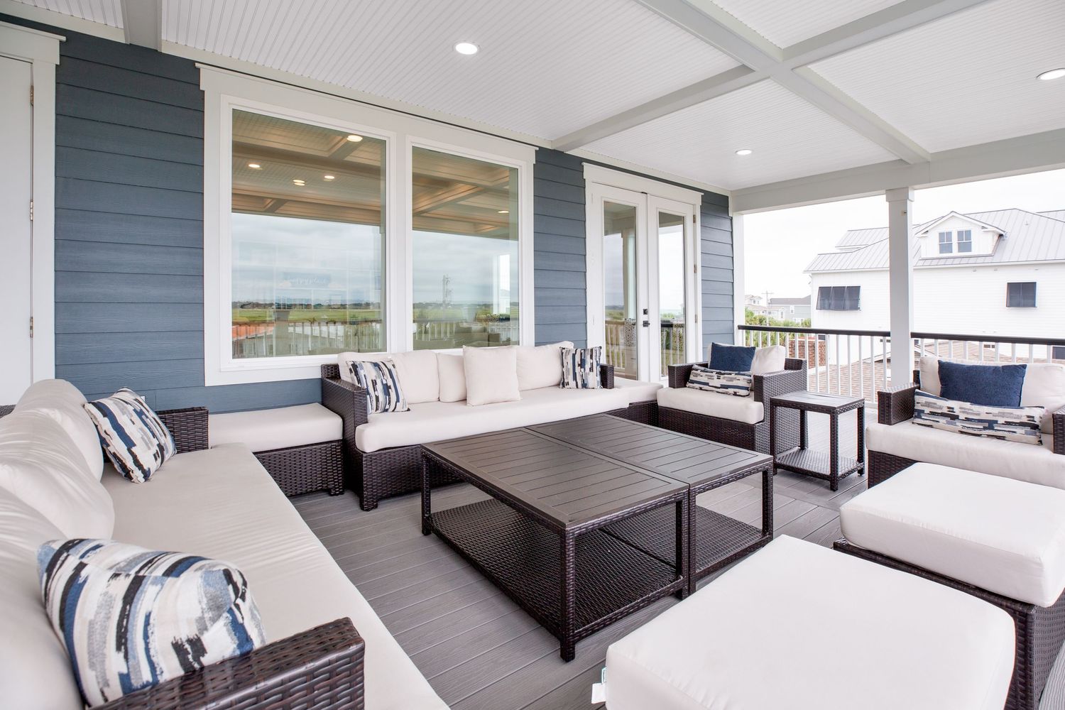 Spacious covered porch with white cushioned wicker furniture and dark wood coffee table.
