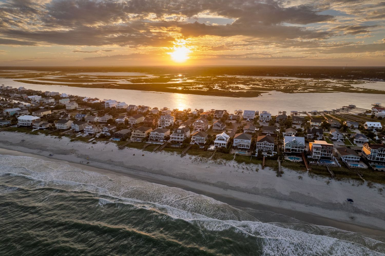 Aerial sunset view of Murrells Inlet and Garden City Beach beachfront homes along a coastal shoreline with ocean waves and golden sky.