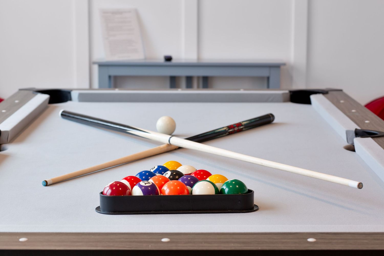 Pool table with colorful billiard balls racked in triangle and two cue sticks ready for play.