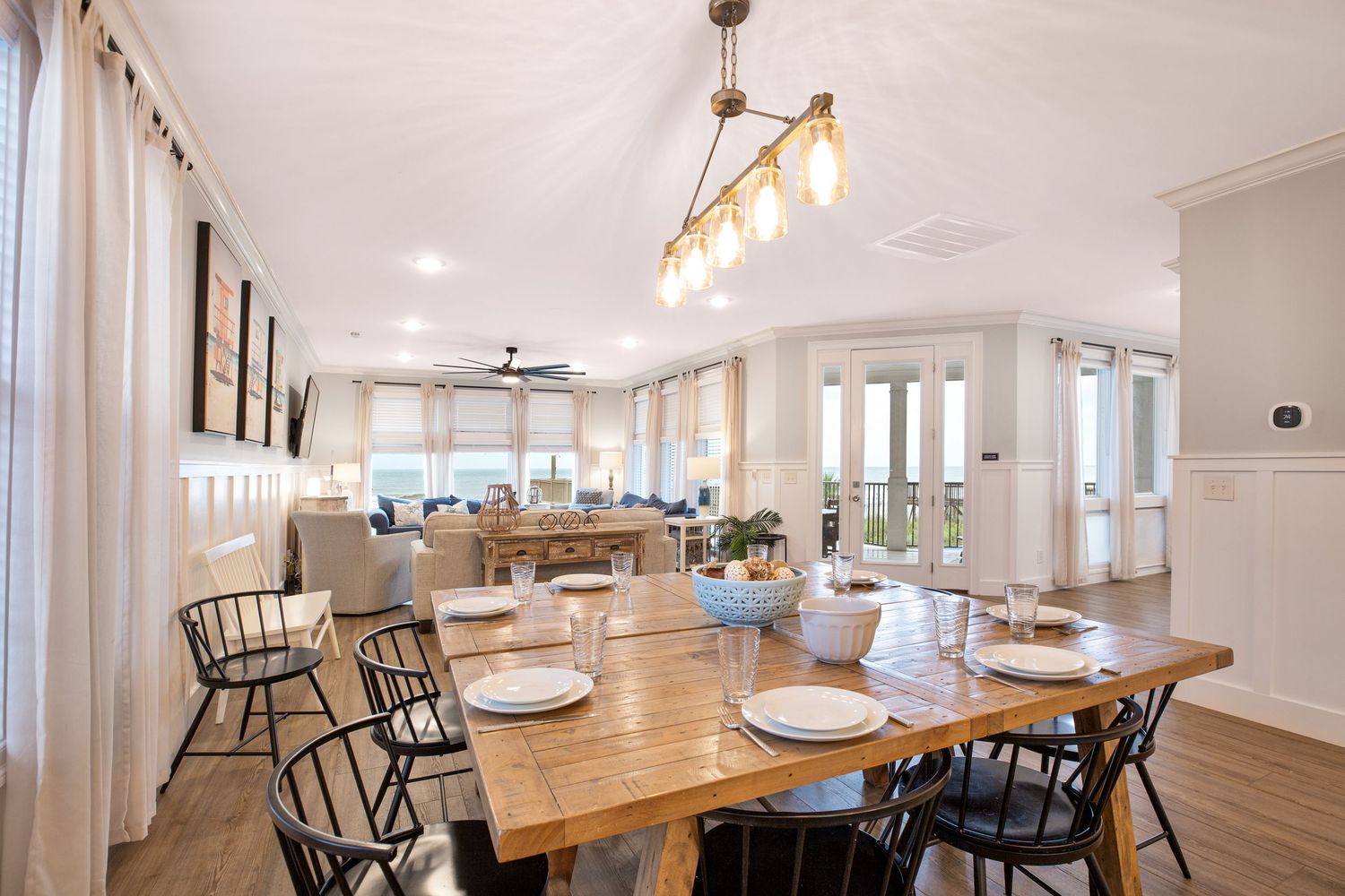 Spacious dining room with wooden farmhouse table, black chairs, vaulted ceiling, and ocean views.