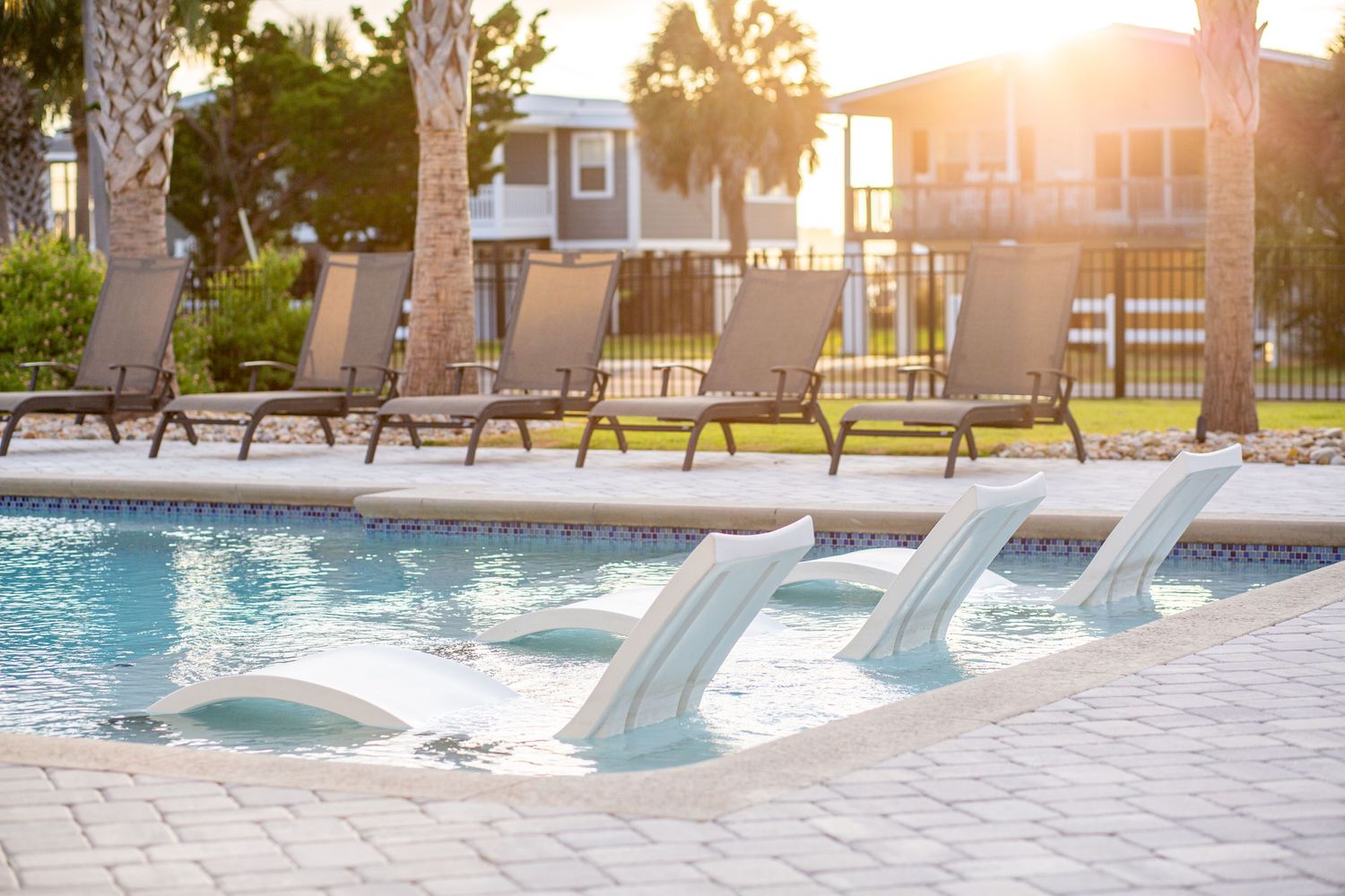 Outdoor resort pool at sunset with lounge chairs, palm trees, and vacation rental homes in the background. Murrells Inlet photographer