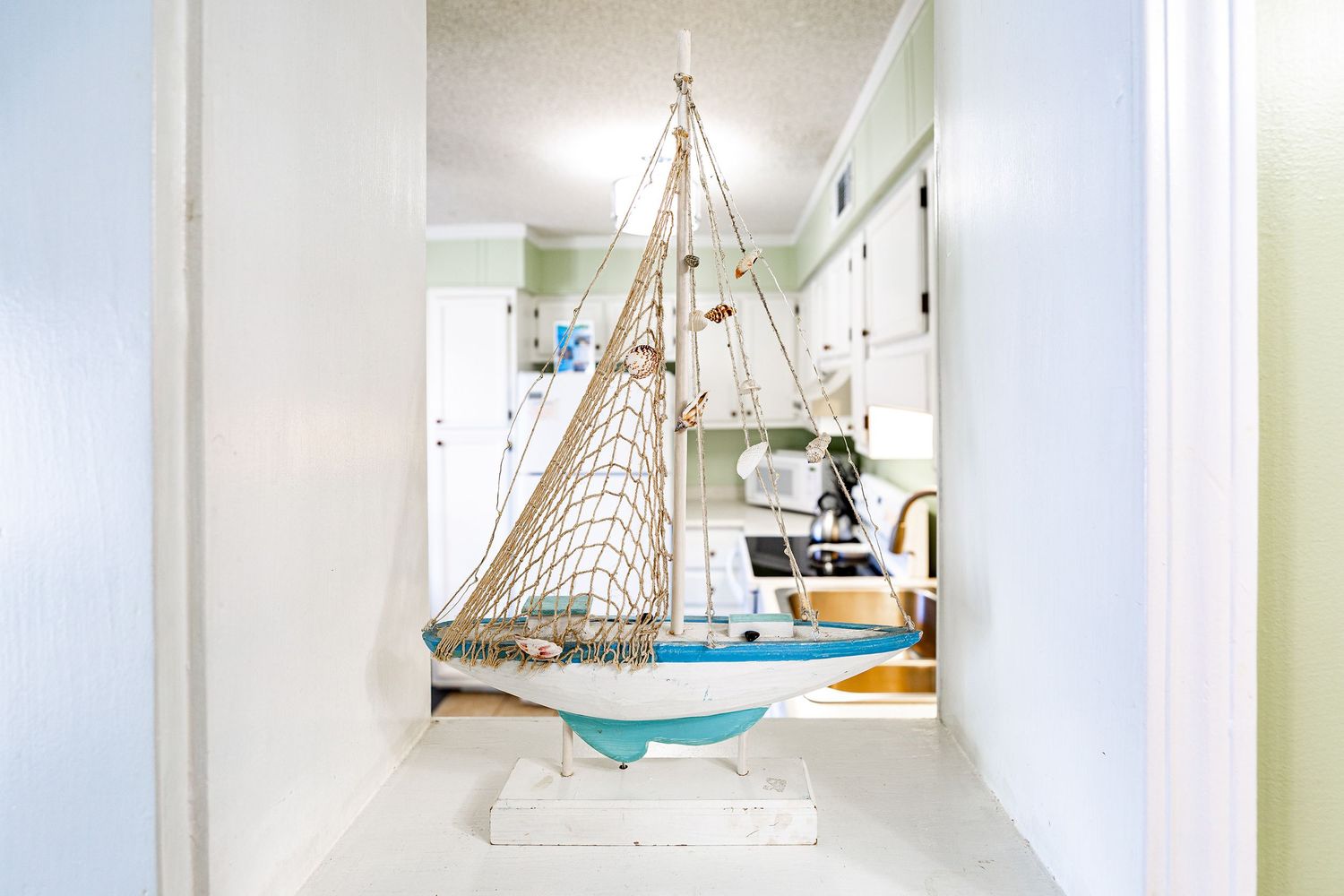 Decorative blue and white sailboat model displayed in a hallway leading to a bright coastal-themed kitchen.