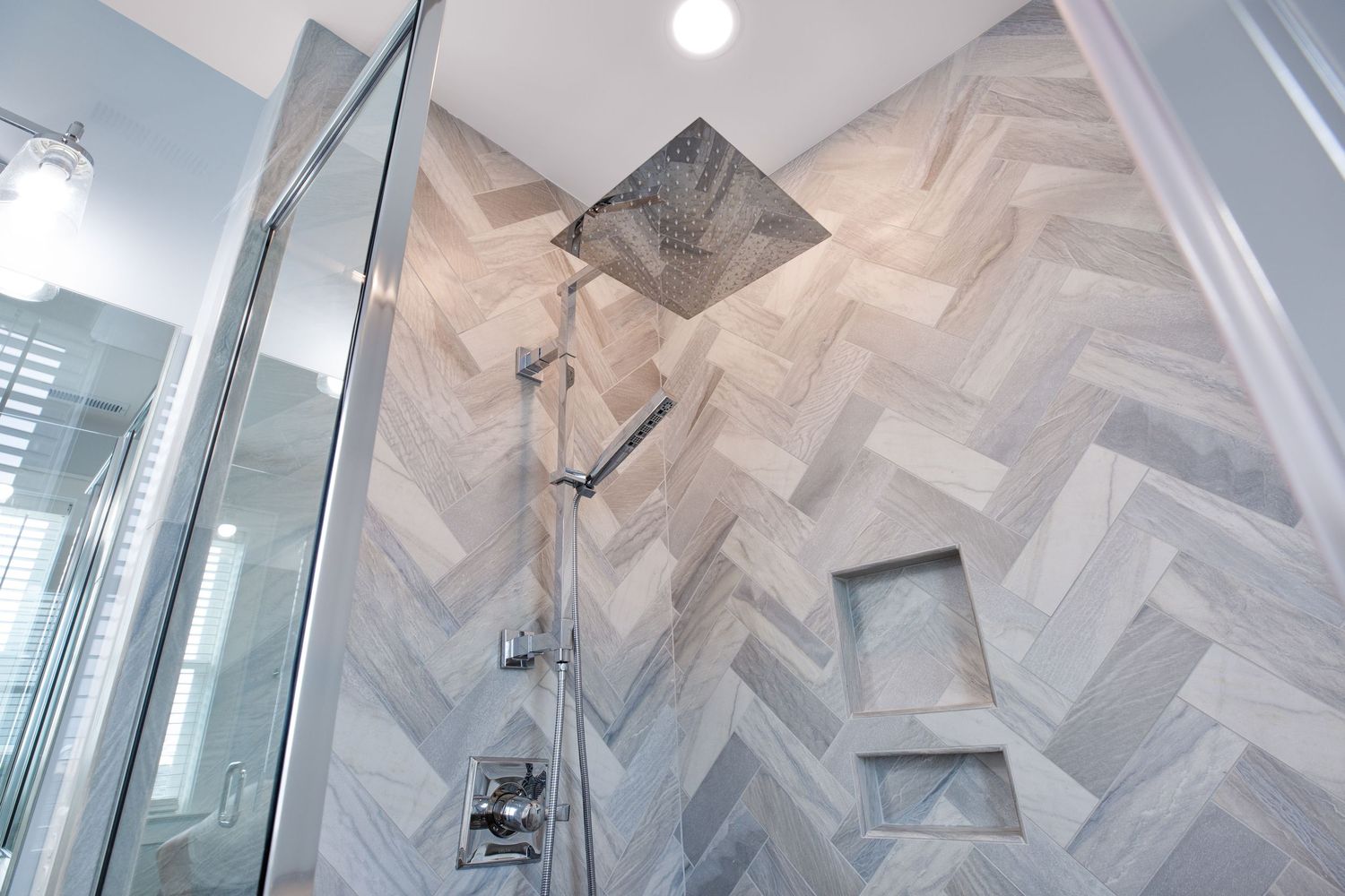 Modern walk-in shower with herringbone tile walls and chrome rainfall showerhead.