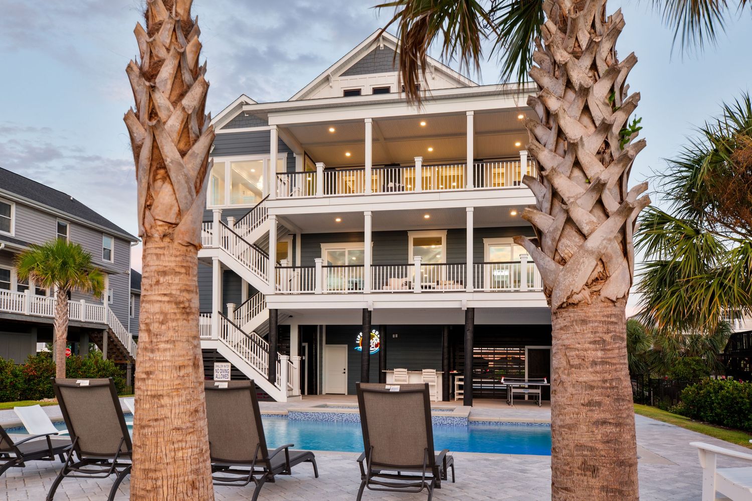 Elegant three-story beach house with private pool, palm trees, and multiple balconies photographed at dusk.