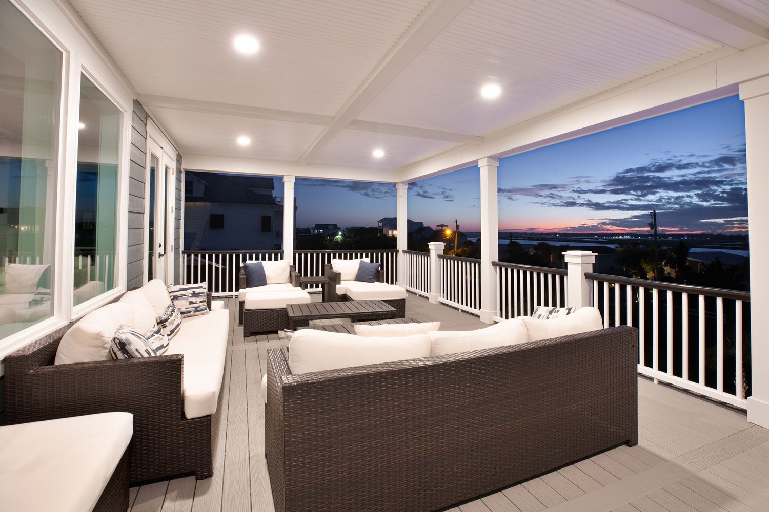 Spacious covered porch with wicker outdoor furniture and panoramic views of a coastal sunset over the Murrells Inlet marshwalk.