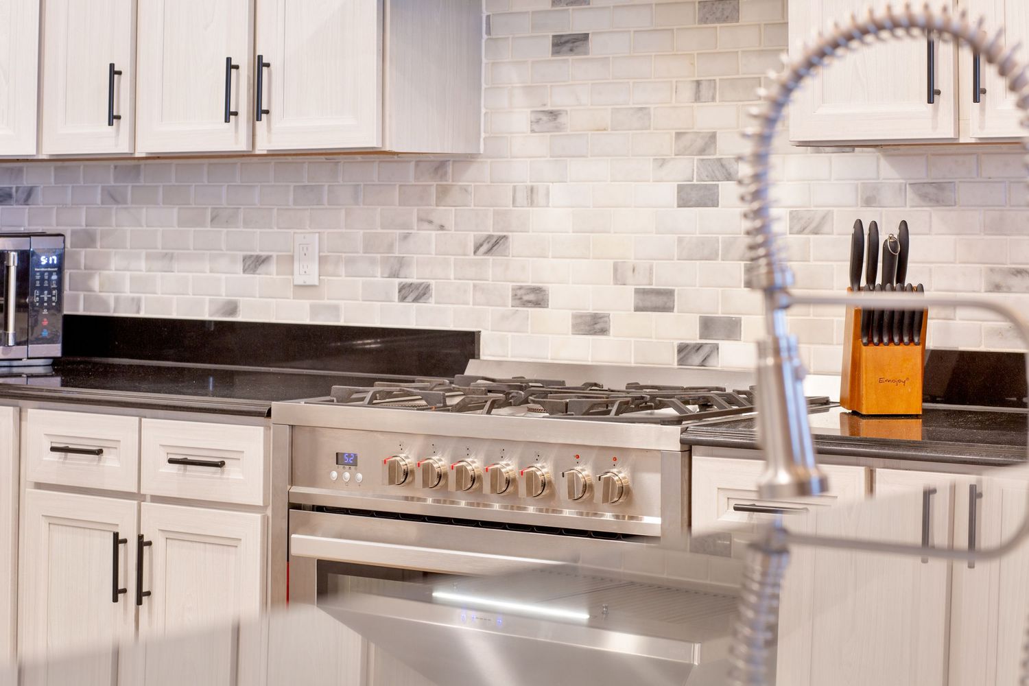 Modern kitchen with white cabinets, marble tile backsplash, stainless steel gas range, and pro faucet.