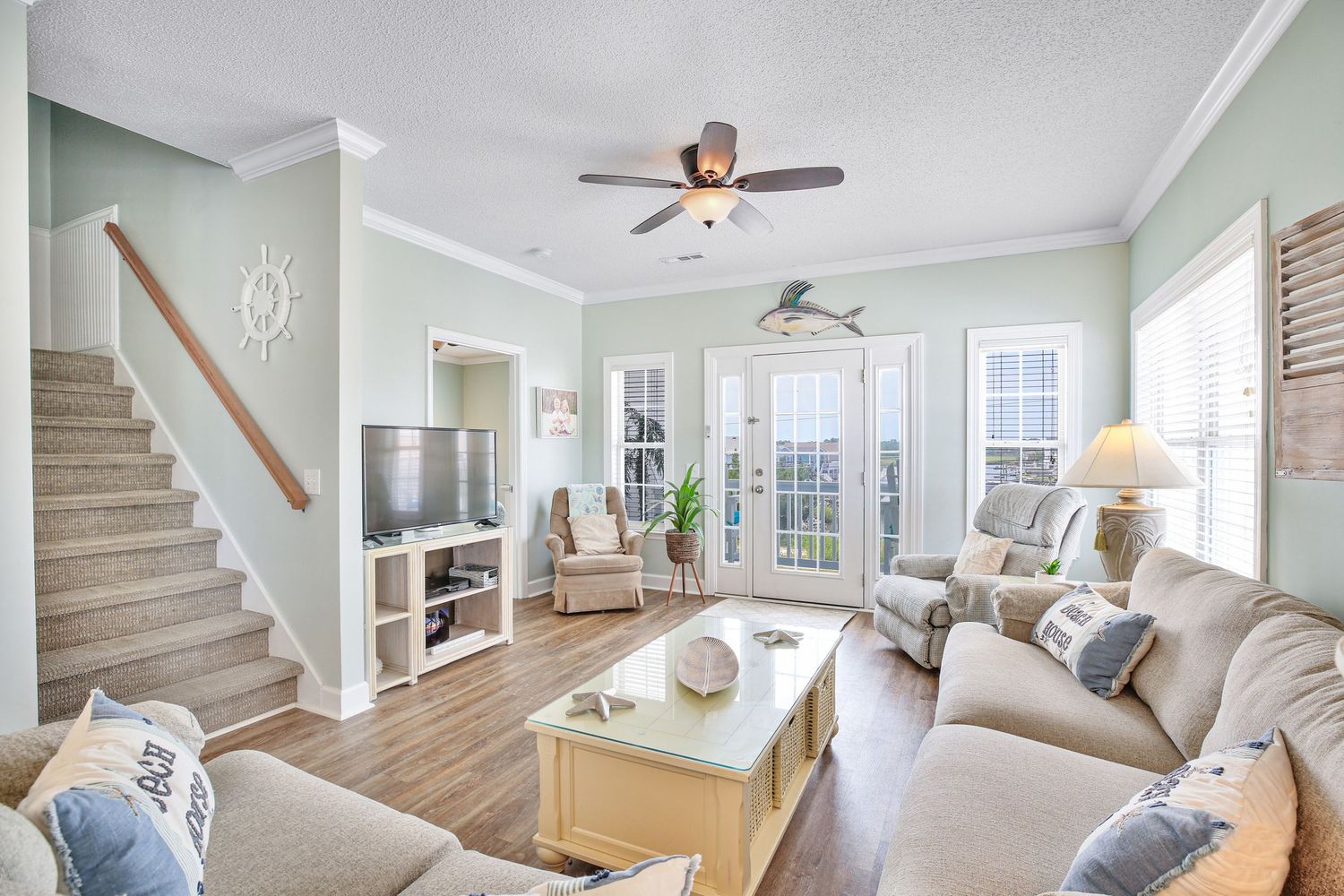 Cozy living room with beige sofas, ceiling fan, staircase, and French doors to outdoor patio.
