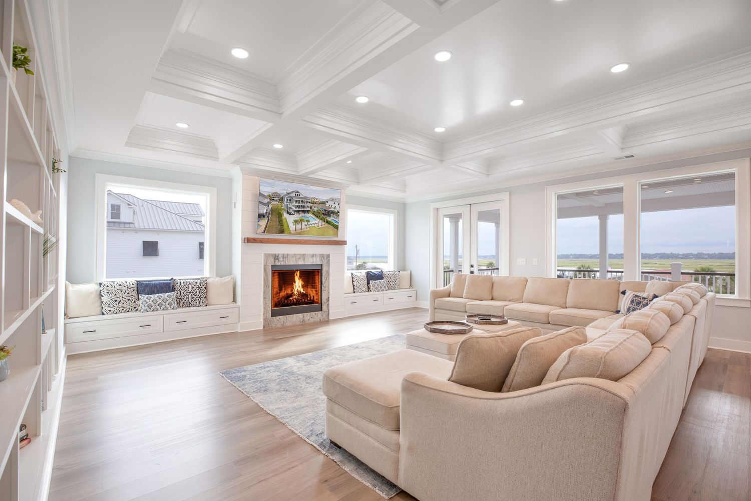 Luxury living room with coffered ceiling, fireplace, large sectional, and ocean views.
