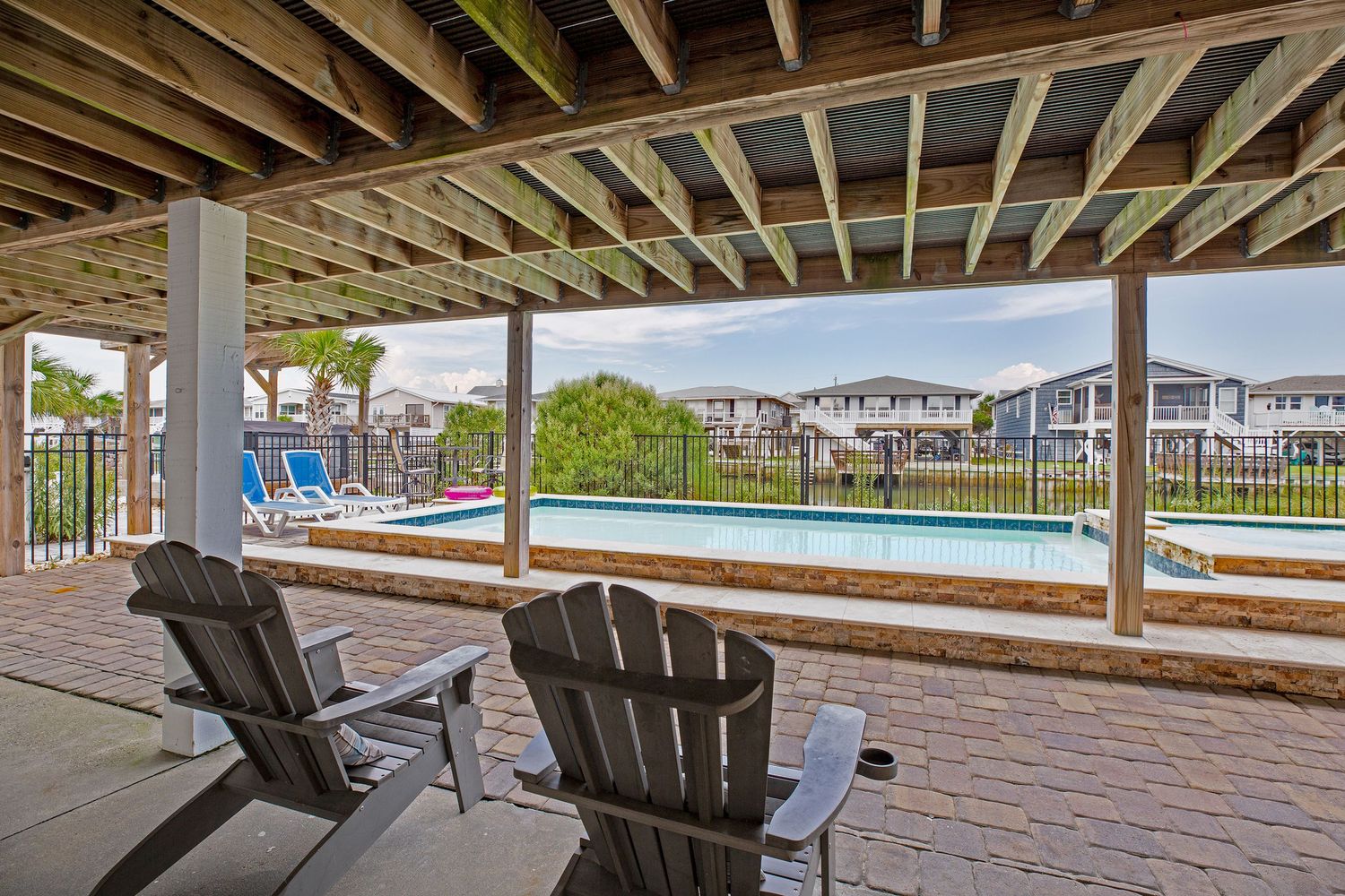 Adirondack chairs on a shaded brick patio overlooking a community pool and neighborhood.