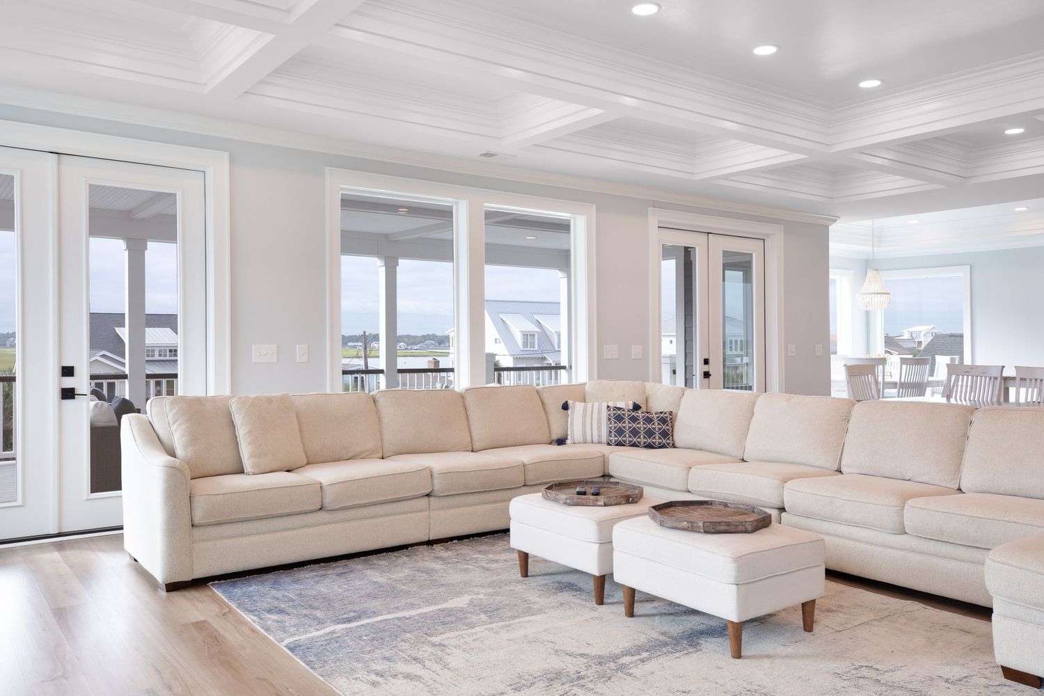 Bright living room with cream sectional sofa, ottomans, and large windows with views.