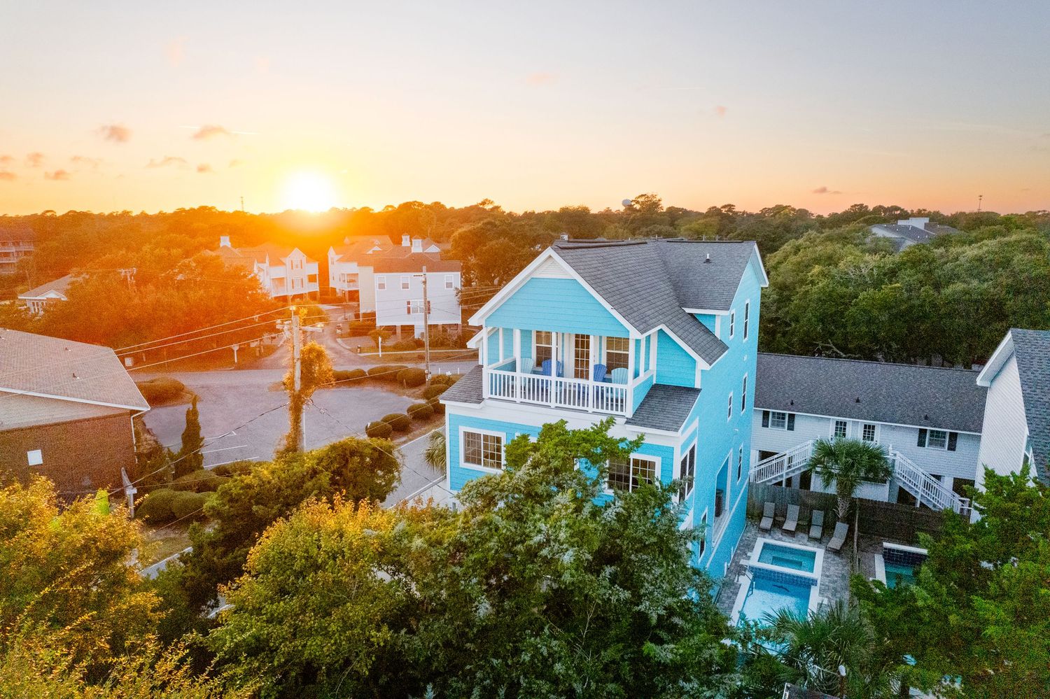 Drone aerial view of a bright blue coastal vacation home with a pool at golden hour sunset. Surfside Beach vacation rental photography