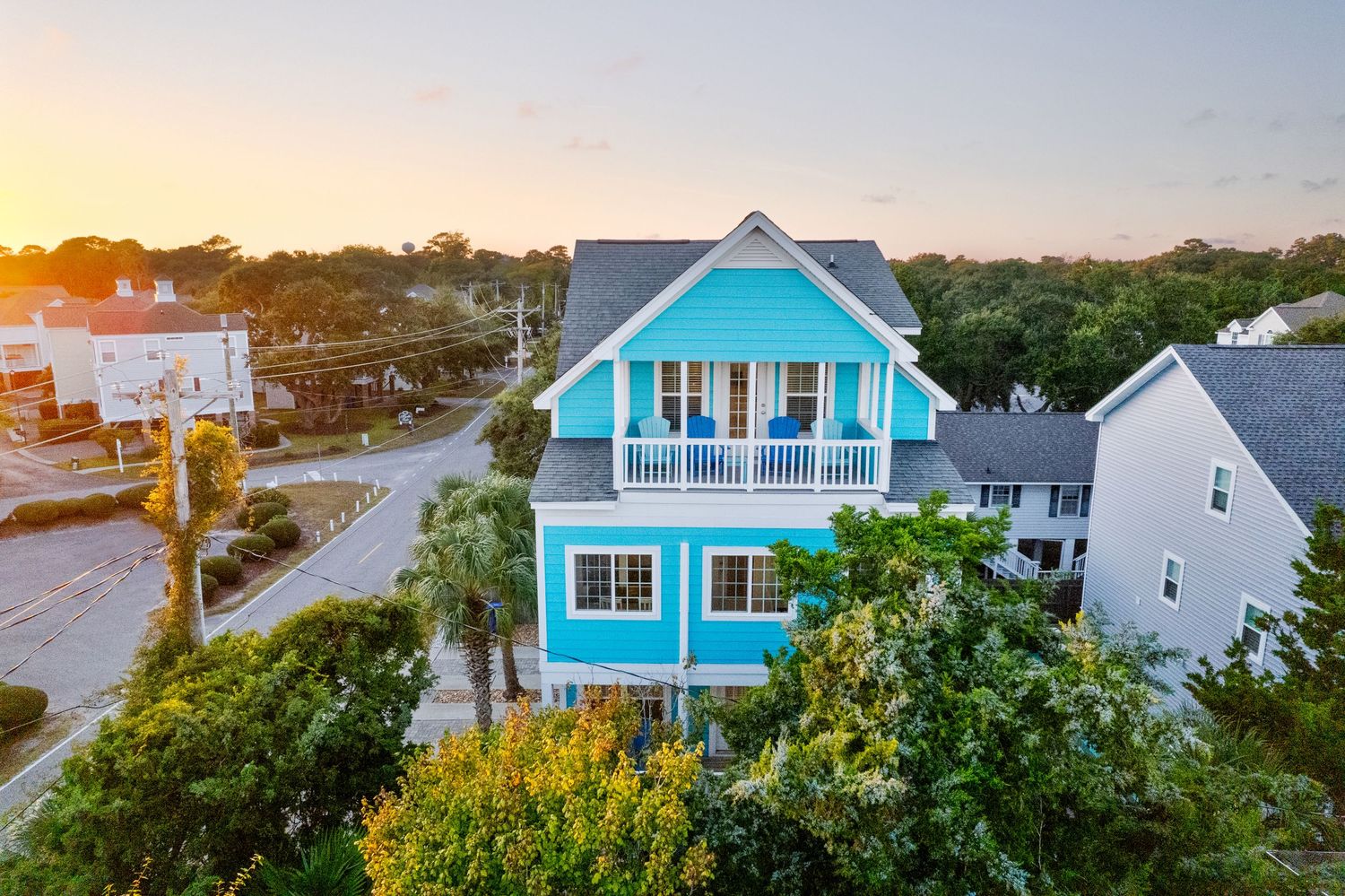 Aerial view of a vibrant turquoise beach house with balconies surrounded by lush trees at sunset in Surfside Beach, SC