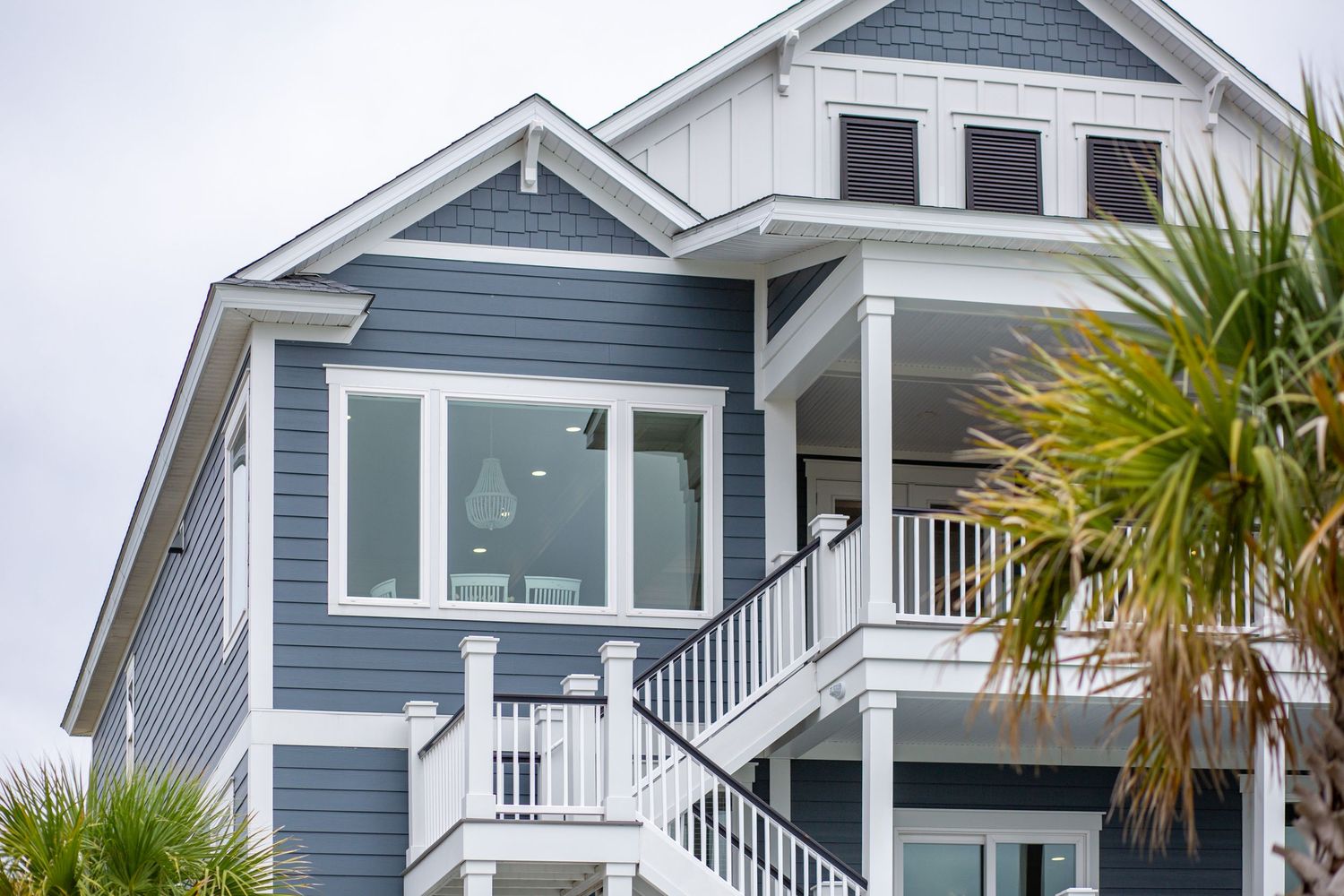 Blue and white coastal beach house exterior with palm tree, white railings, and exterior staircase.