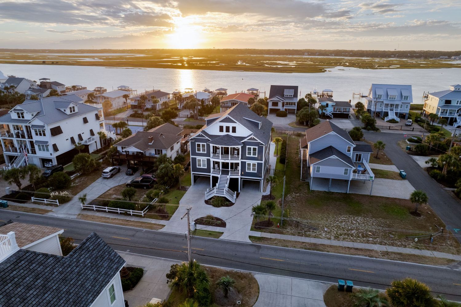 Aerial sunset view of a large coastal vacation home near sparkling waterways in a beachside residential neighborhood.