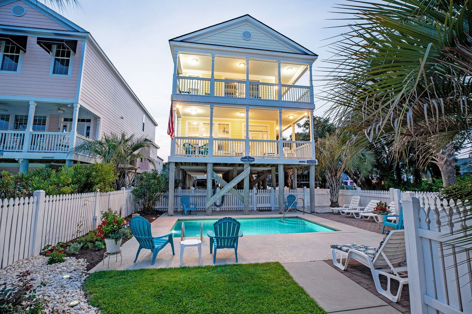 Three-story beach house in Surfside Beach SC, exterior at dusk with private pool, lounge chairs, and lush landscaping.