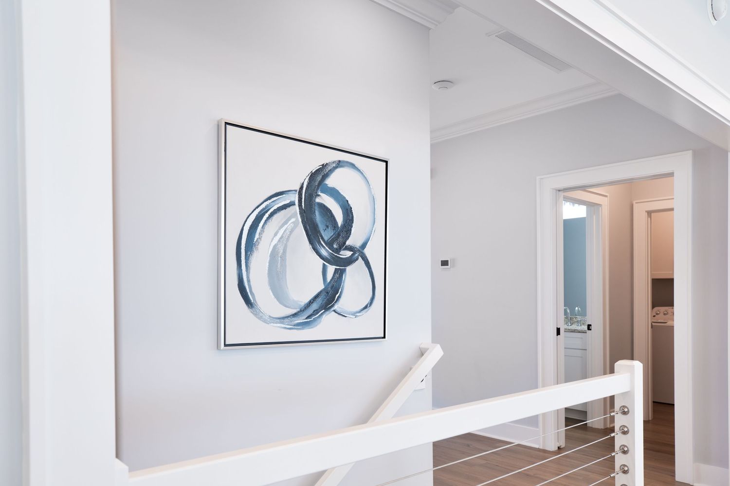 Bright hallway with abstract blue circular wall art above white stair railing.