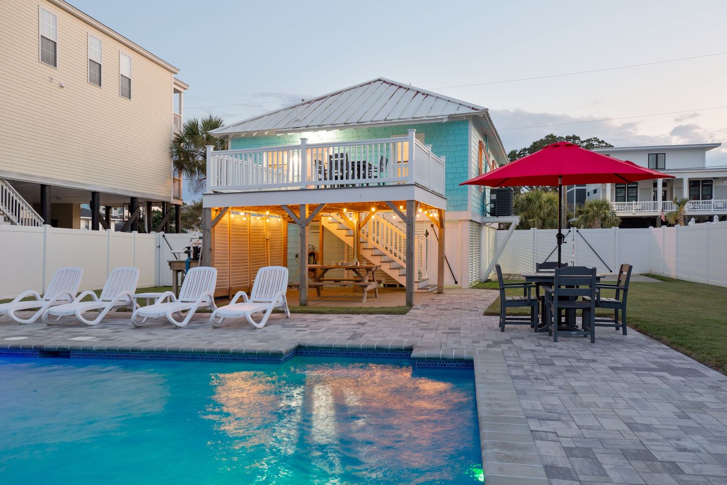 Private pool and patio area behind a charming two-story beach house with lounge chairs.