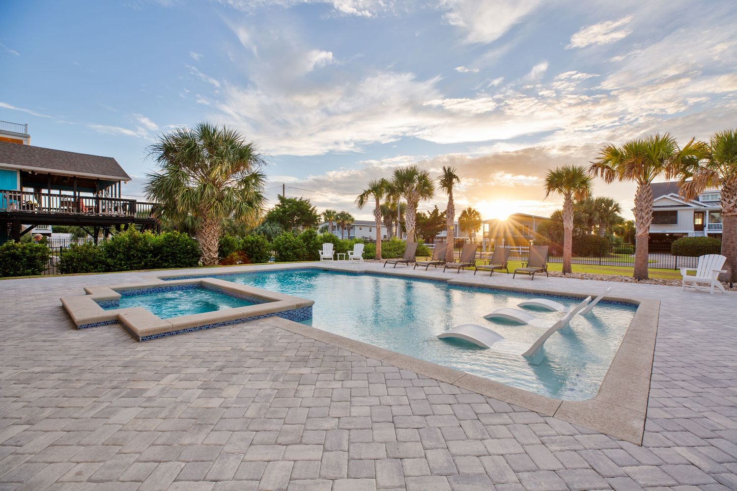 Stunning private outdoor pool and hot tub at sunset surrounded by palm trees and multi-story beach vacation homes.