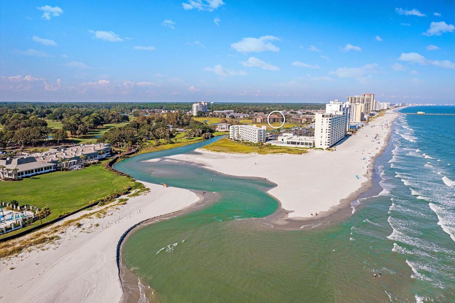 Aerial view of the Singleton Swash with a tall beachfront condominium tower beside a tidal inlet and Dunes golf course.
