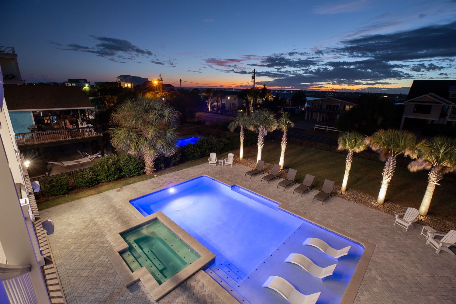 Illuminated luxury pool and hot tub at twilight with palm trees and colorful sunset sky at a beach resort.