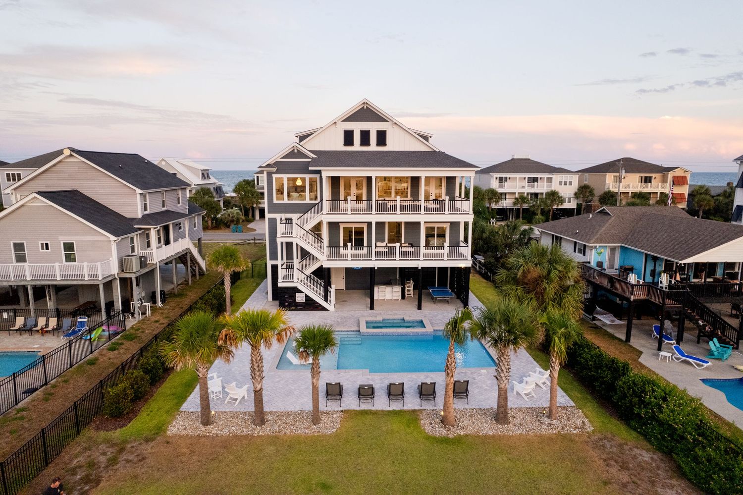 Luxury multi-story beach house with private pool, palm trees, and spacious deck at dusk.