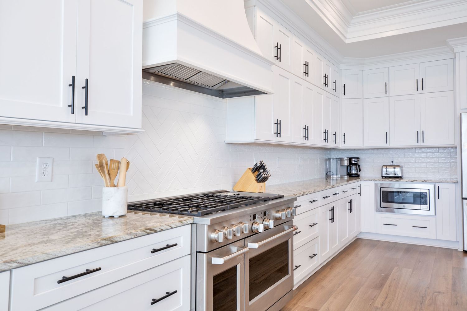 Bright white kitchen with shaker cabinets, granite countertops, and stainless steel range.