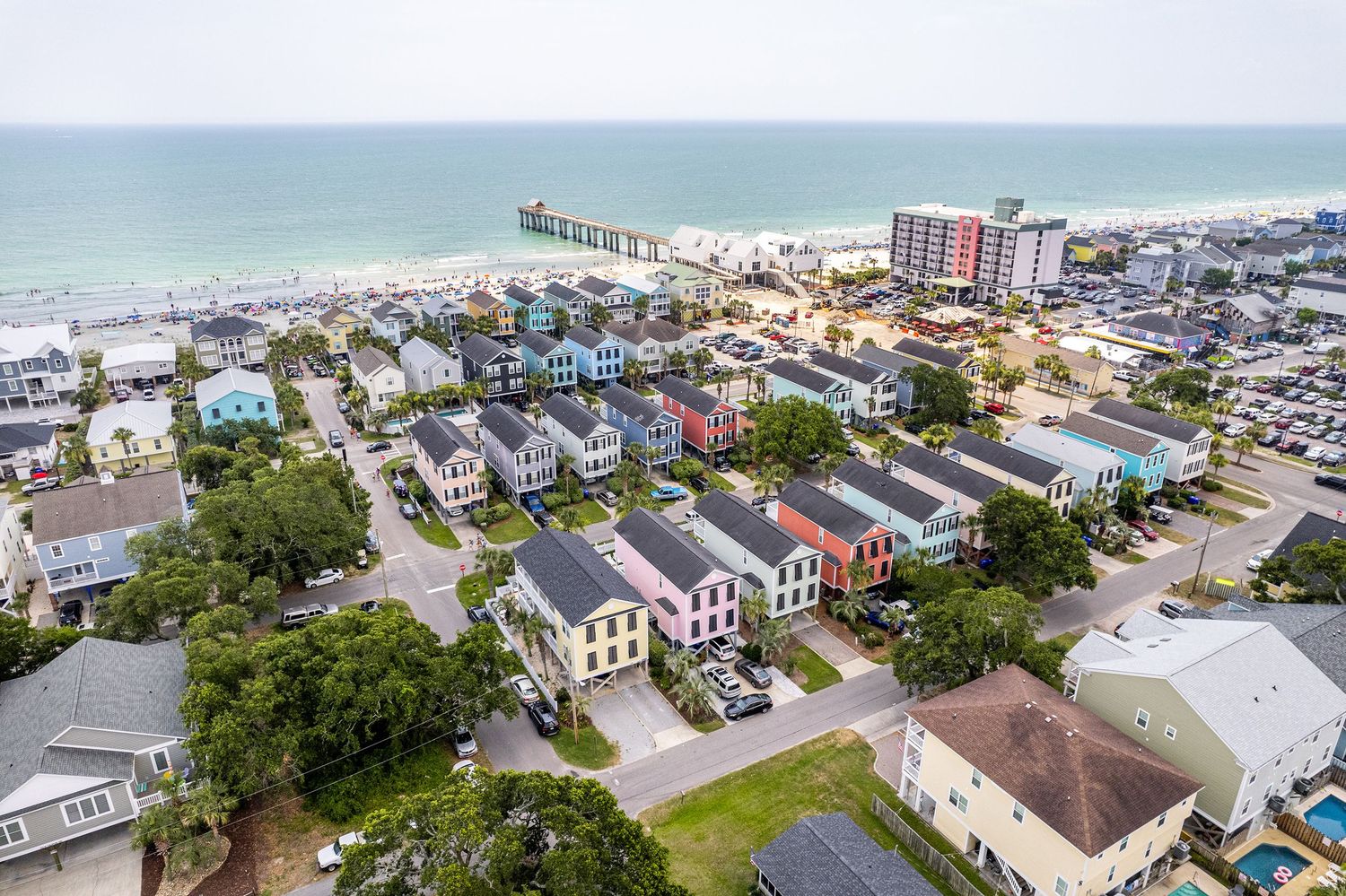 Aerial view of colorful beachside homes and condos near the Surfside Pier with the ocean and sandy beach in the background.