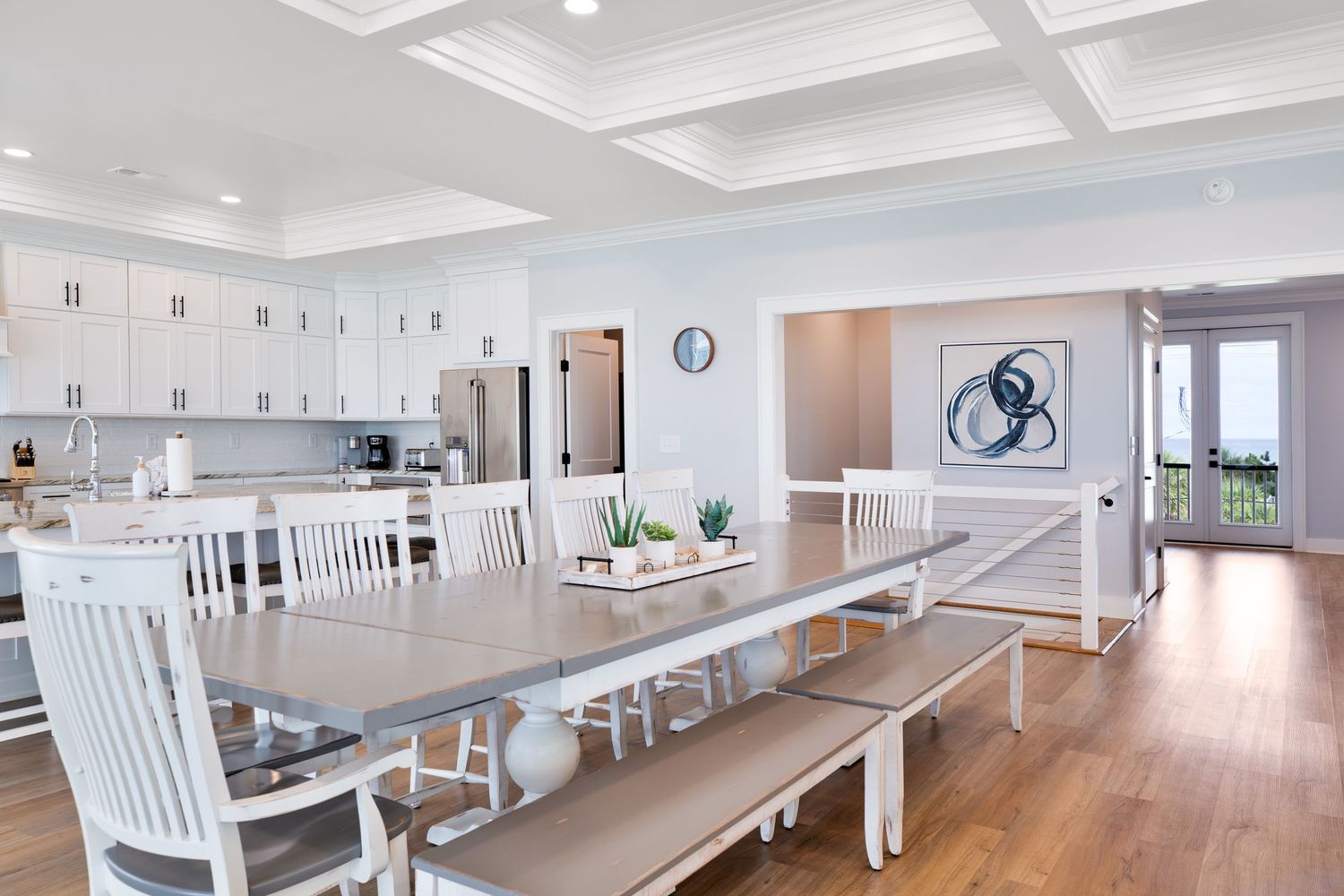 Open dining room with long farmhouse table, white chairs, bench, and kitchen beyond.