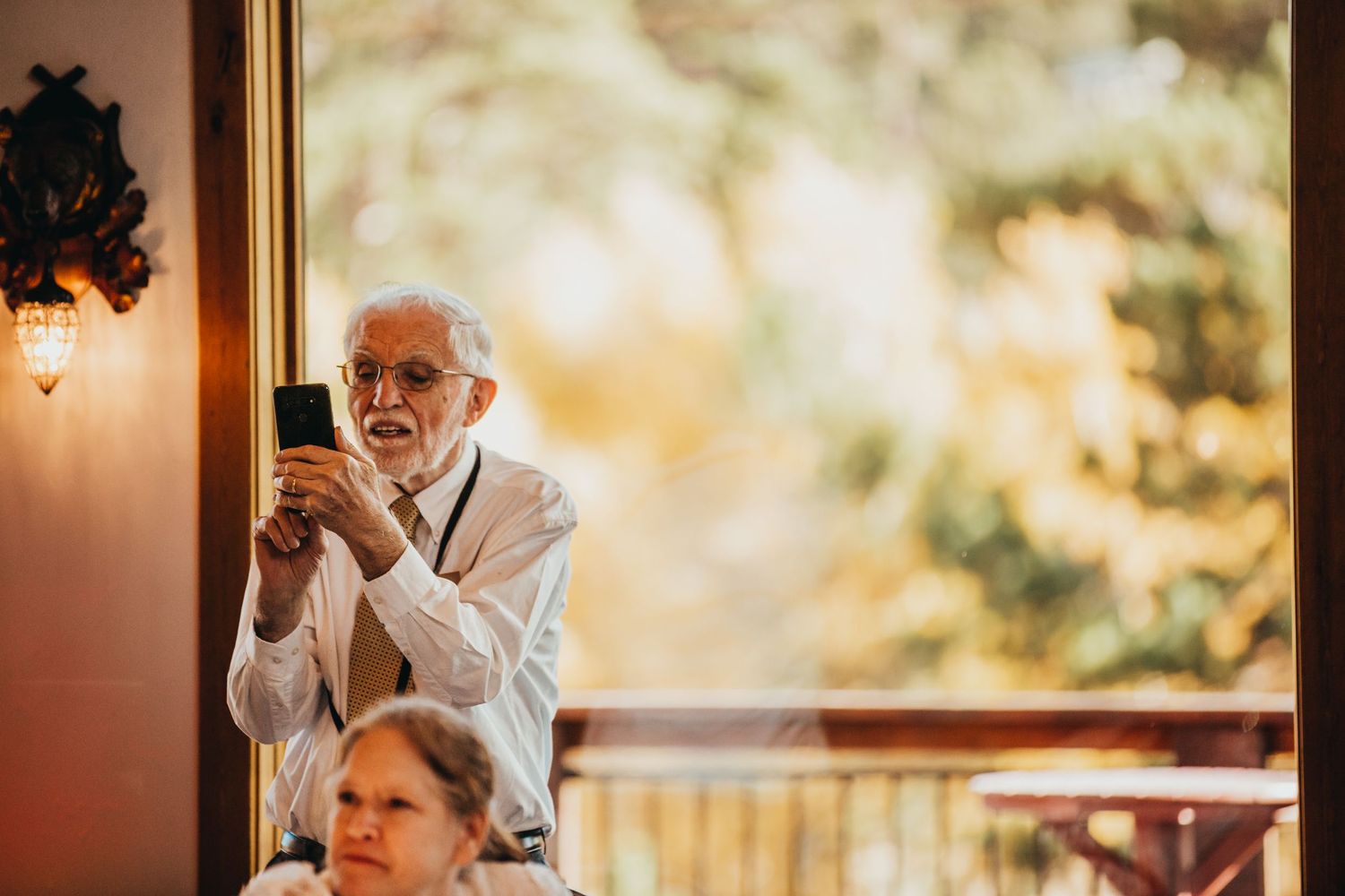 An elderly guest takes a photo with their phone during a wedding reception.
