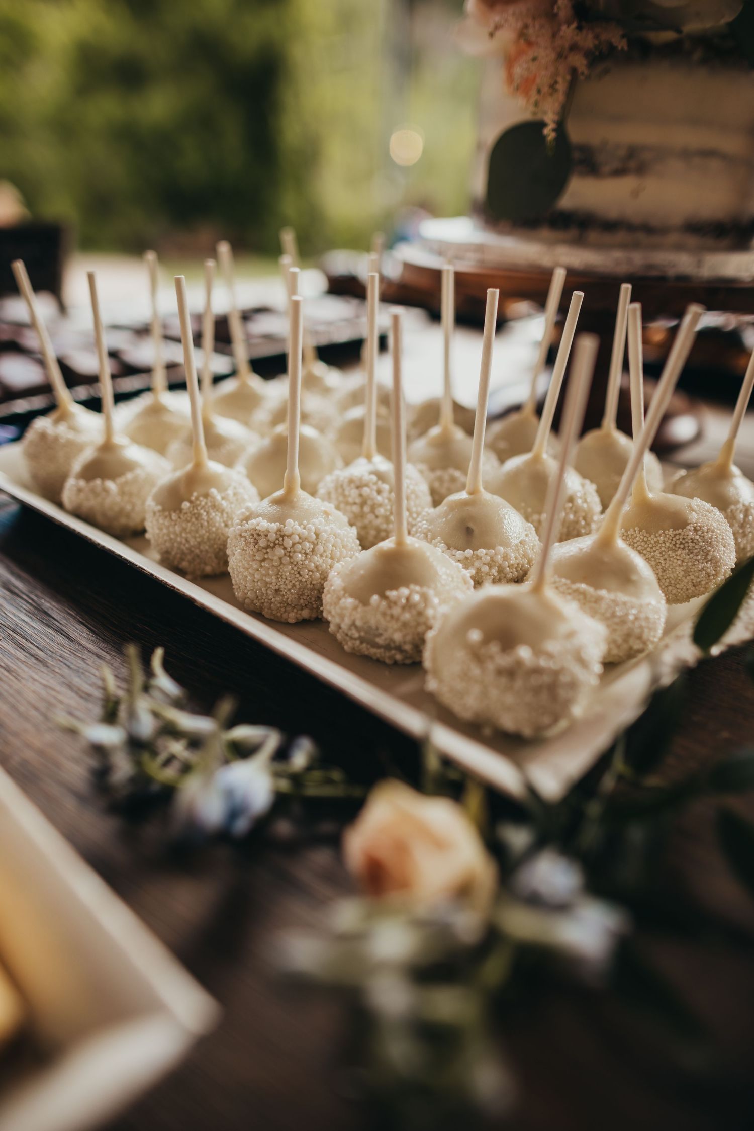 Elegant cake pops decorated in white with sparkly sugar displayed on a rustic wooden dessert table.