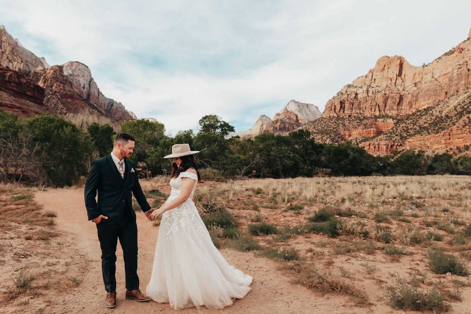 Wedding couple poses against stunning red rock formations in a desert landscape at sunset.