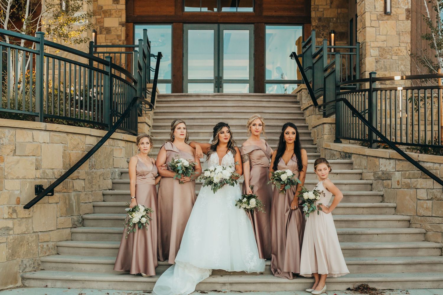 Bridesmaids in rose-colored dresses pose with the bride on grand stone steps.