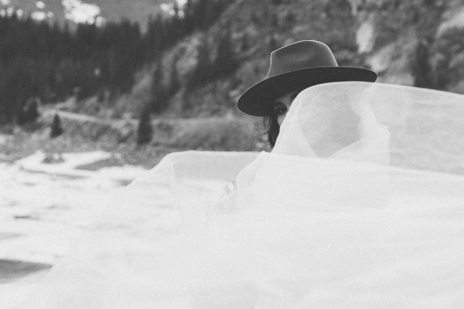 Artistic black and white close-up of a wide-brim hat and veil against mountain scenery.