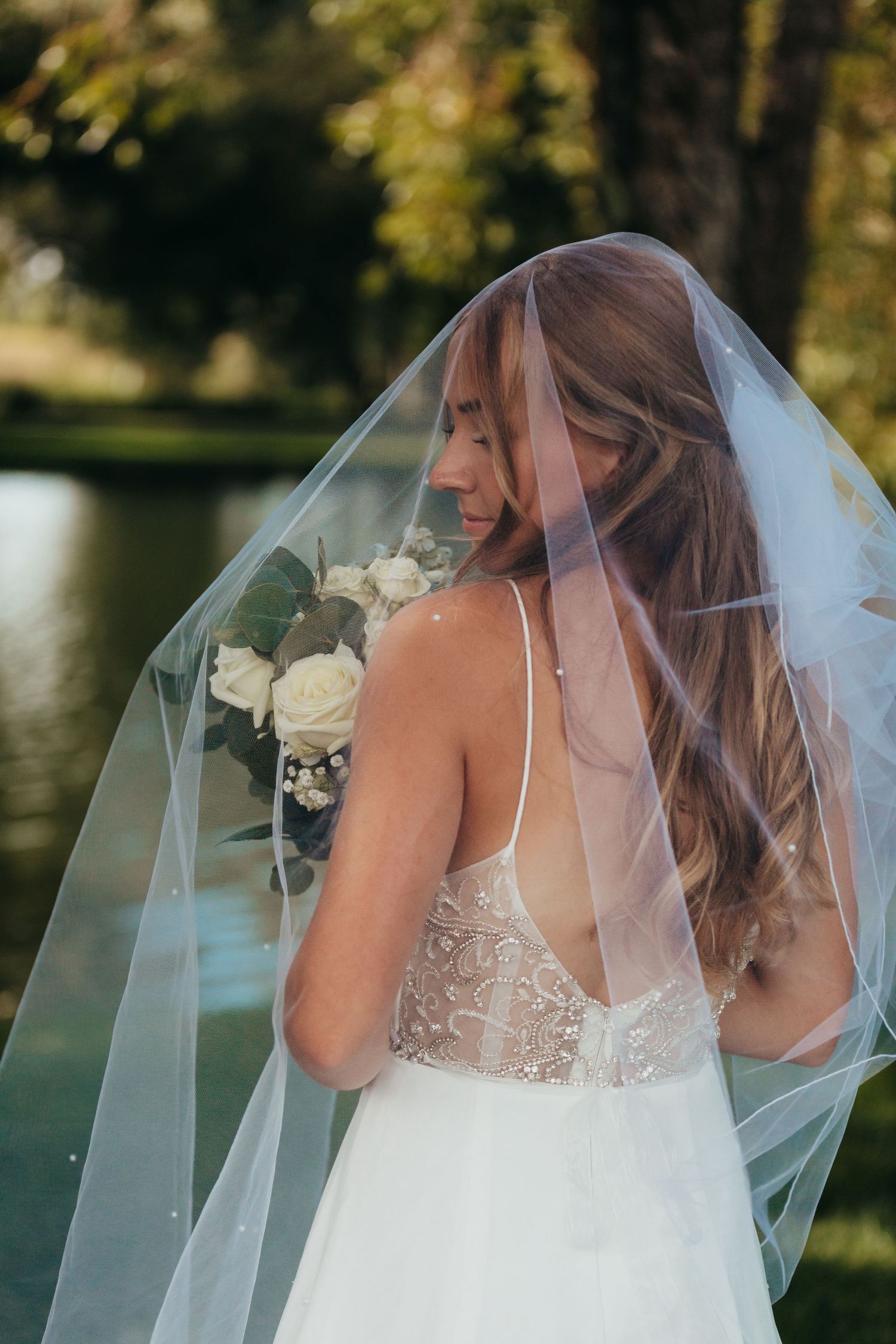 Back view of lace wedding dress with sheer veil against natural outdoor setting.