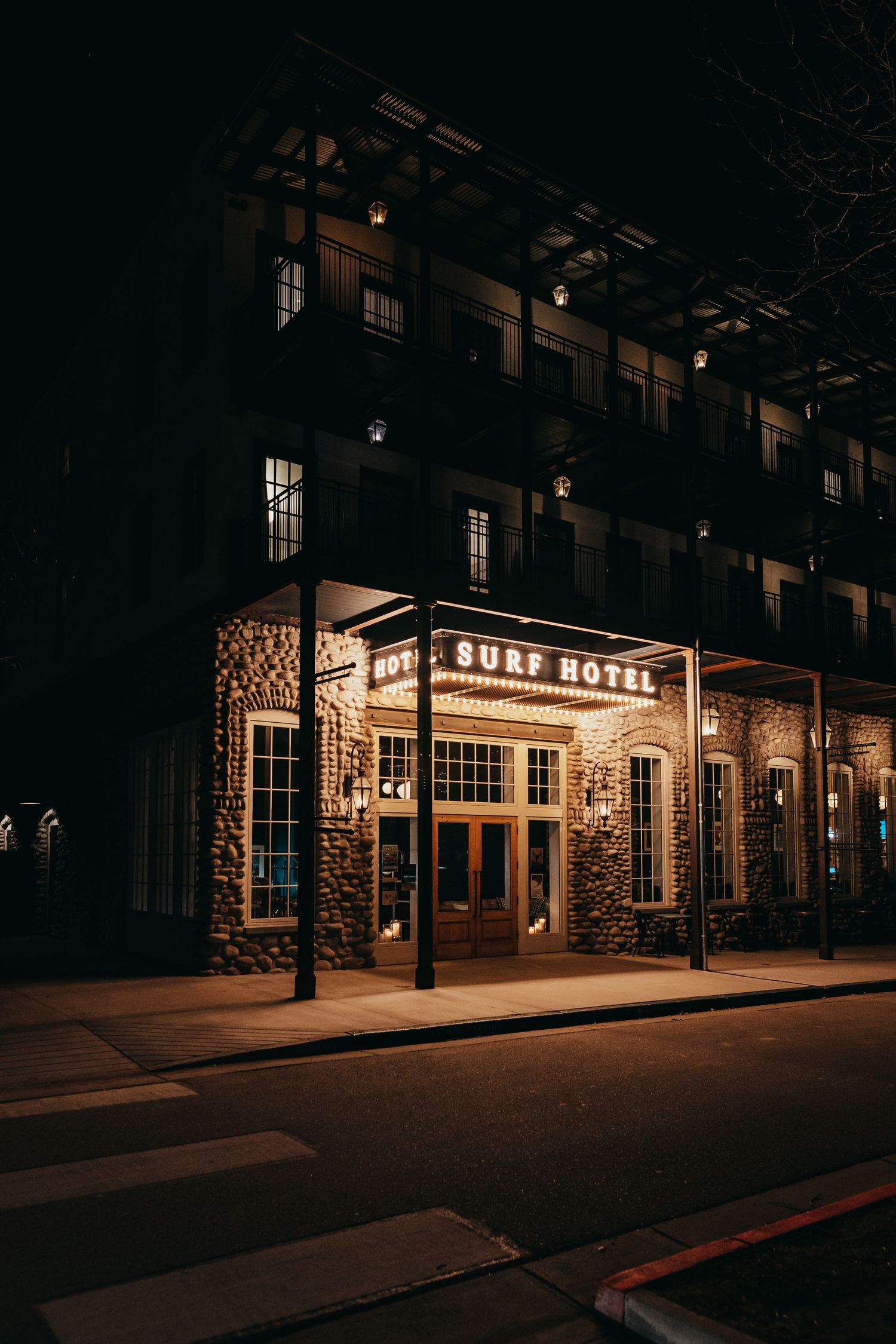 Exterior night view of the historic Surf Hotel with illuminated signage and stone facade.