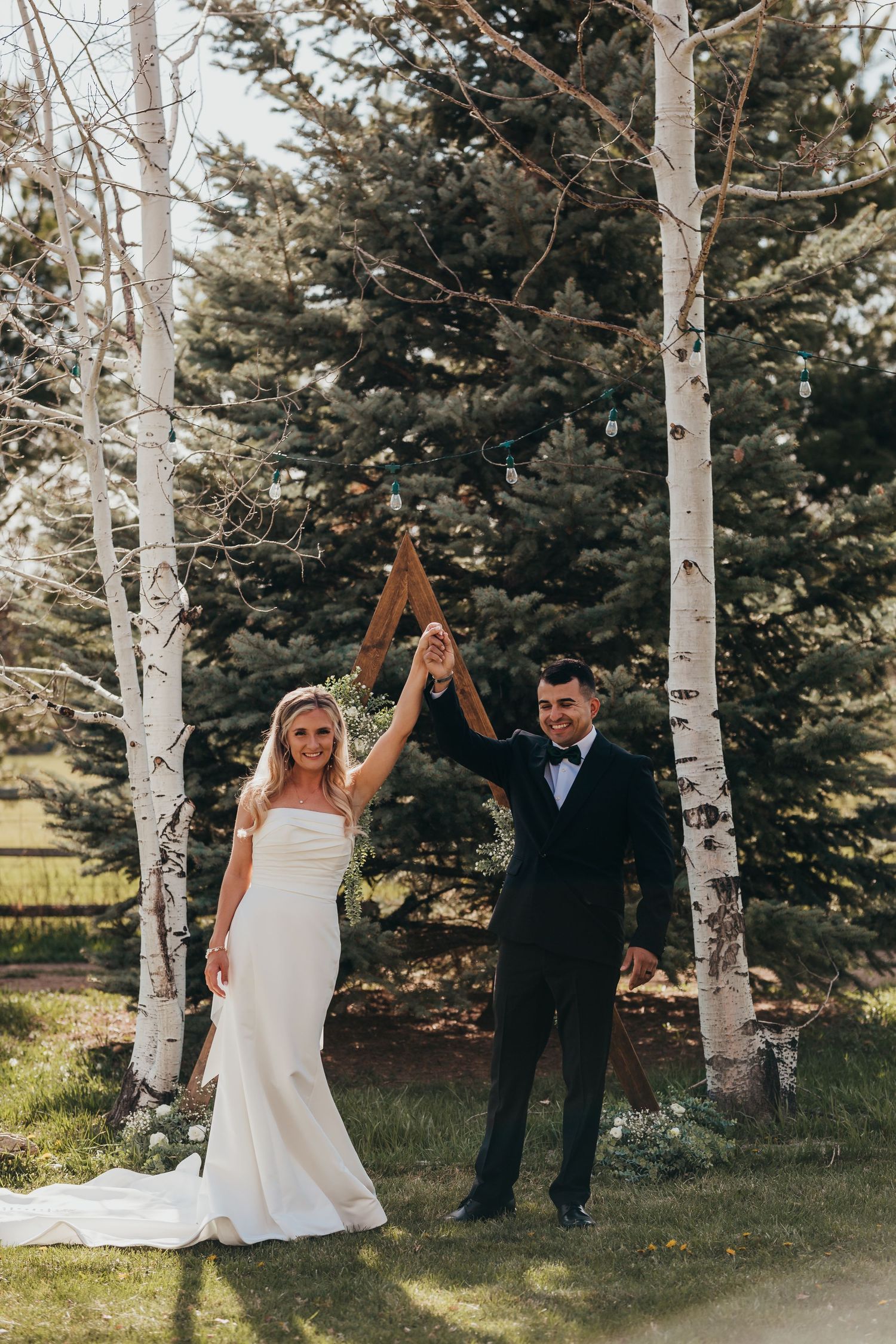 Newlyweds celebrating with raised hands between white birch trees in an outdoor setting.
