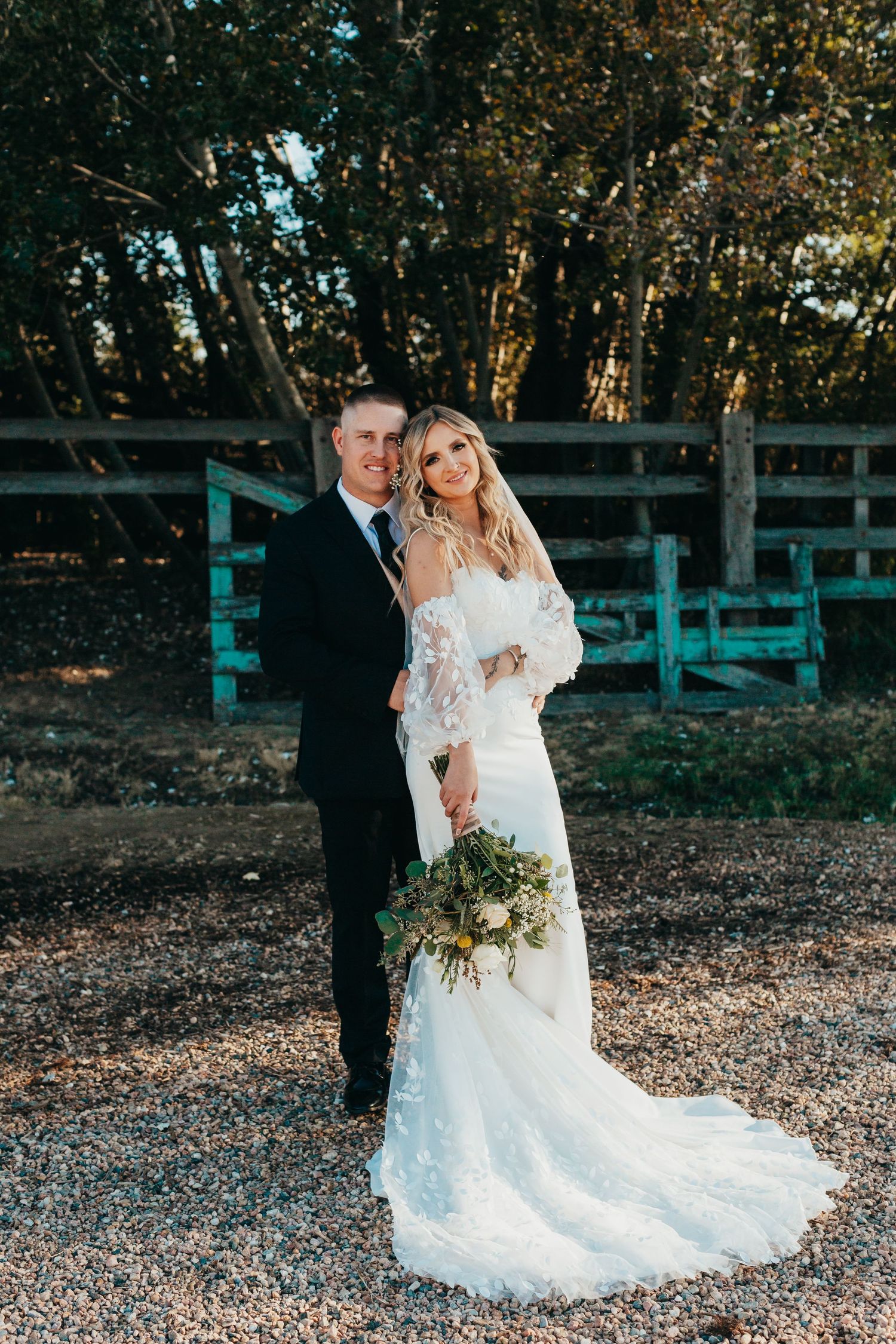 A romantic wedding portrait of newlyweds posing together against rustic wooden fence backdrop.