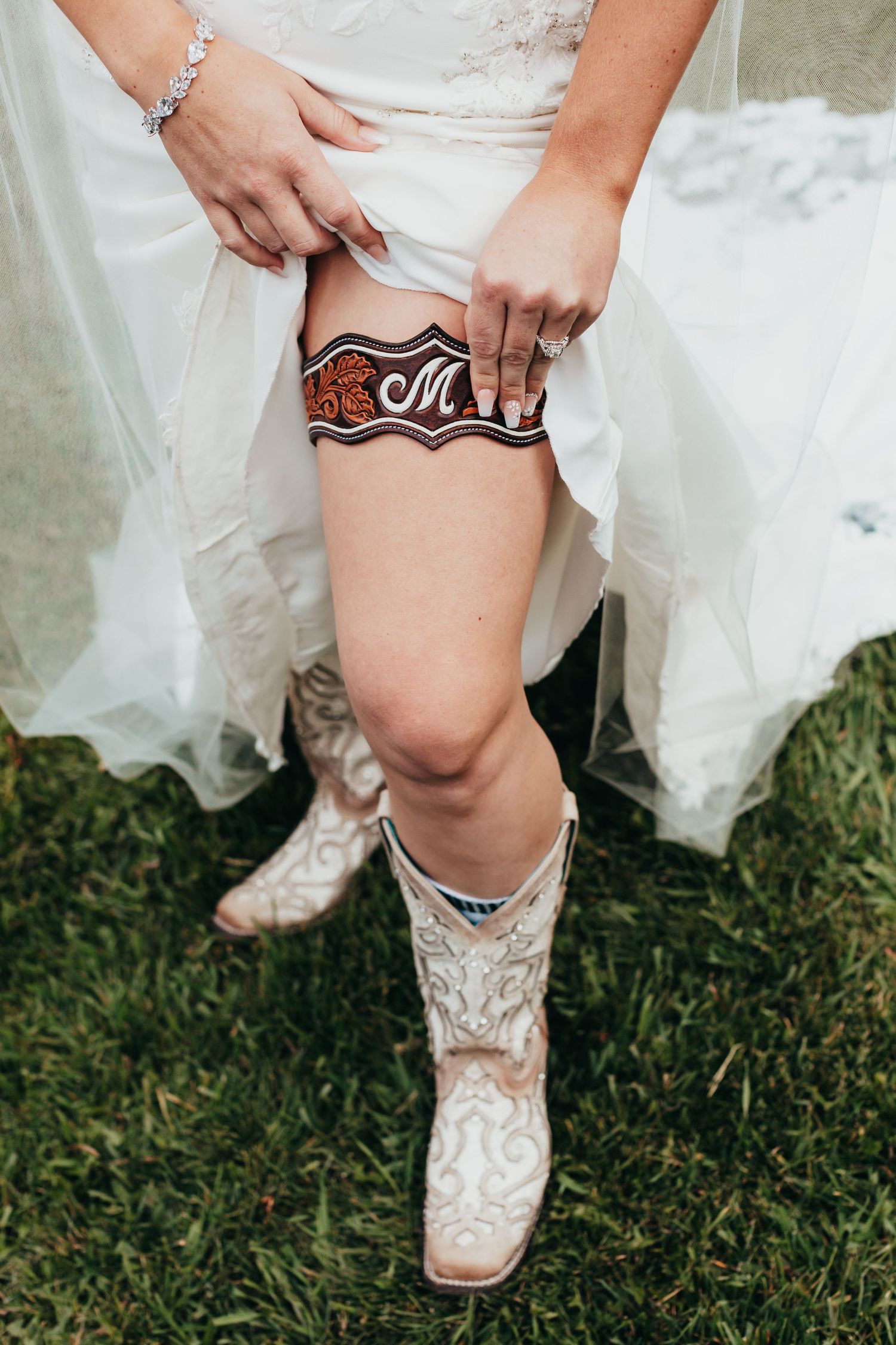A close-up of cowboy boots and a garter worn under a white wedding dress.