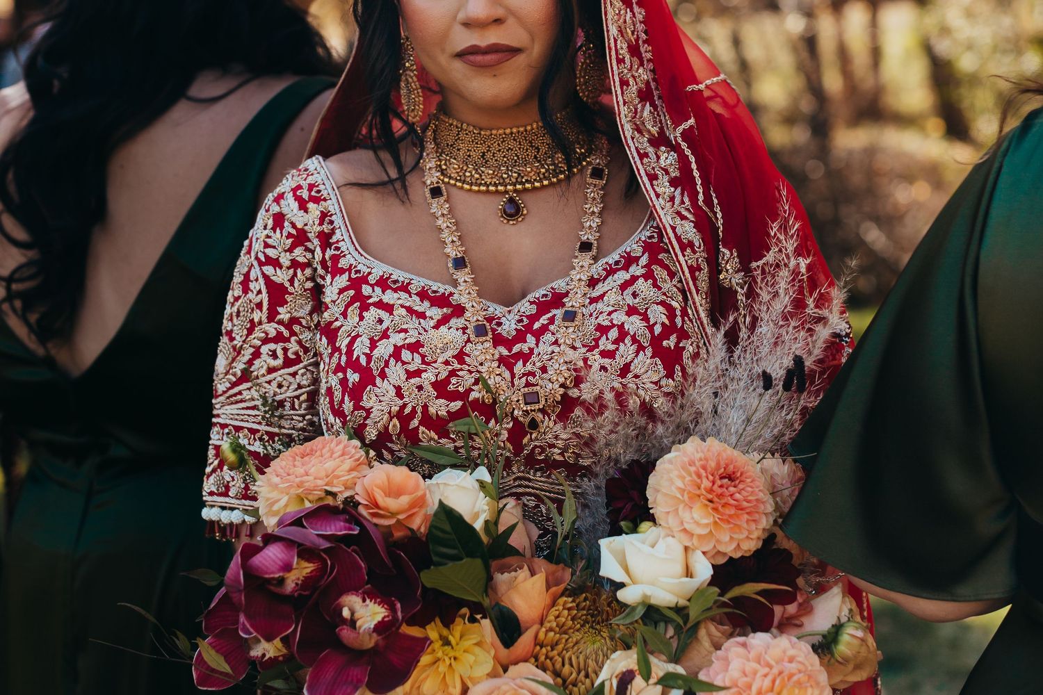 Close-up of bridal bouquet with coral and purple flowers against intricate red wedding attire.