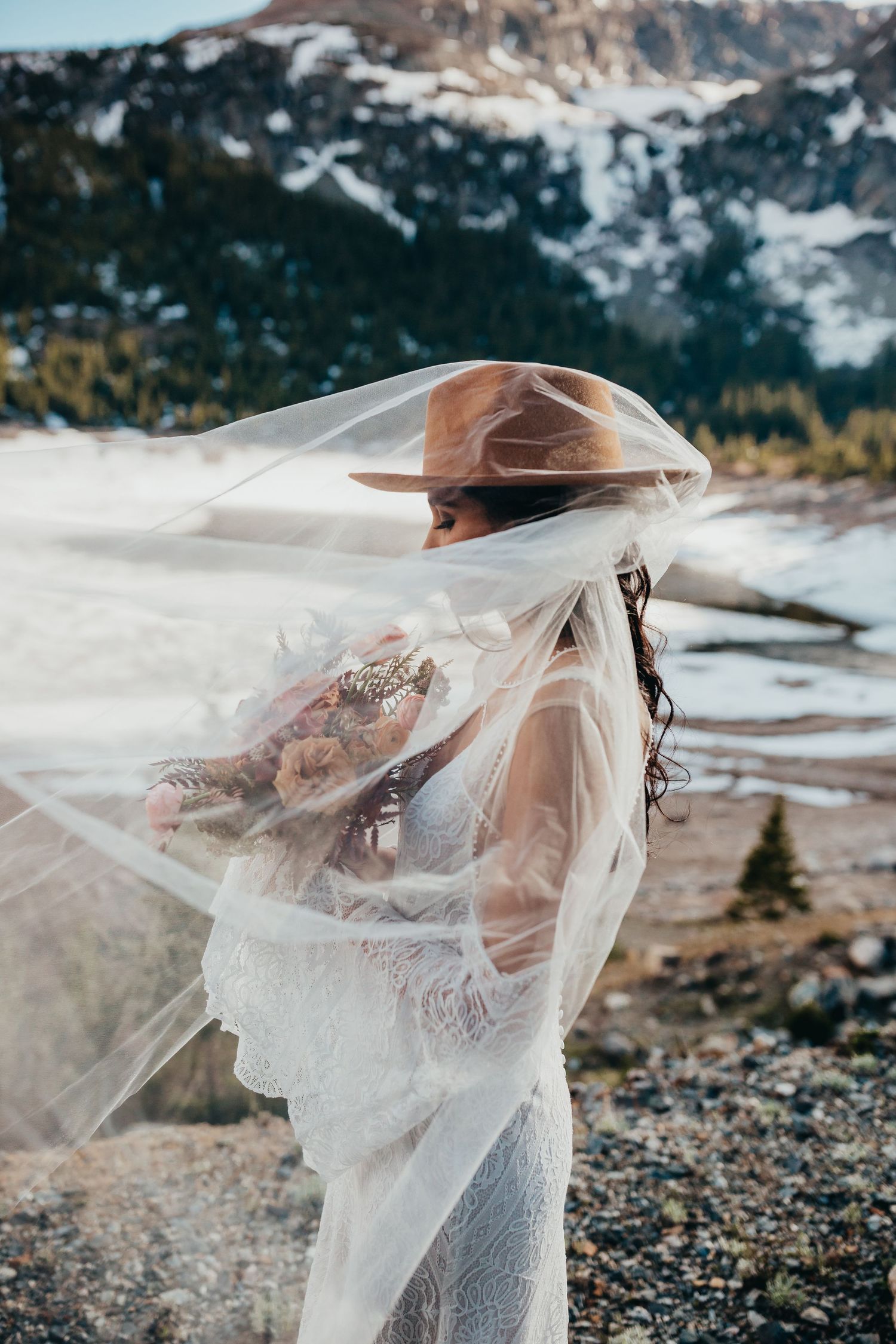 A delicate wedding veil flows in the wind against a snowy mountain backdrop.
