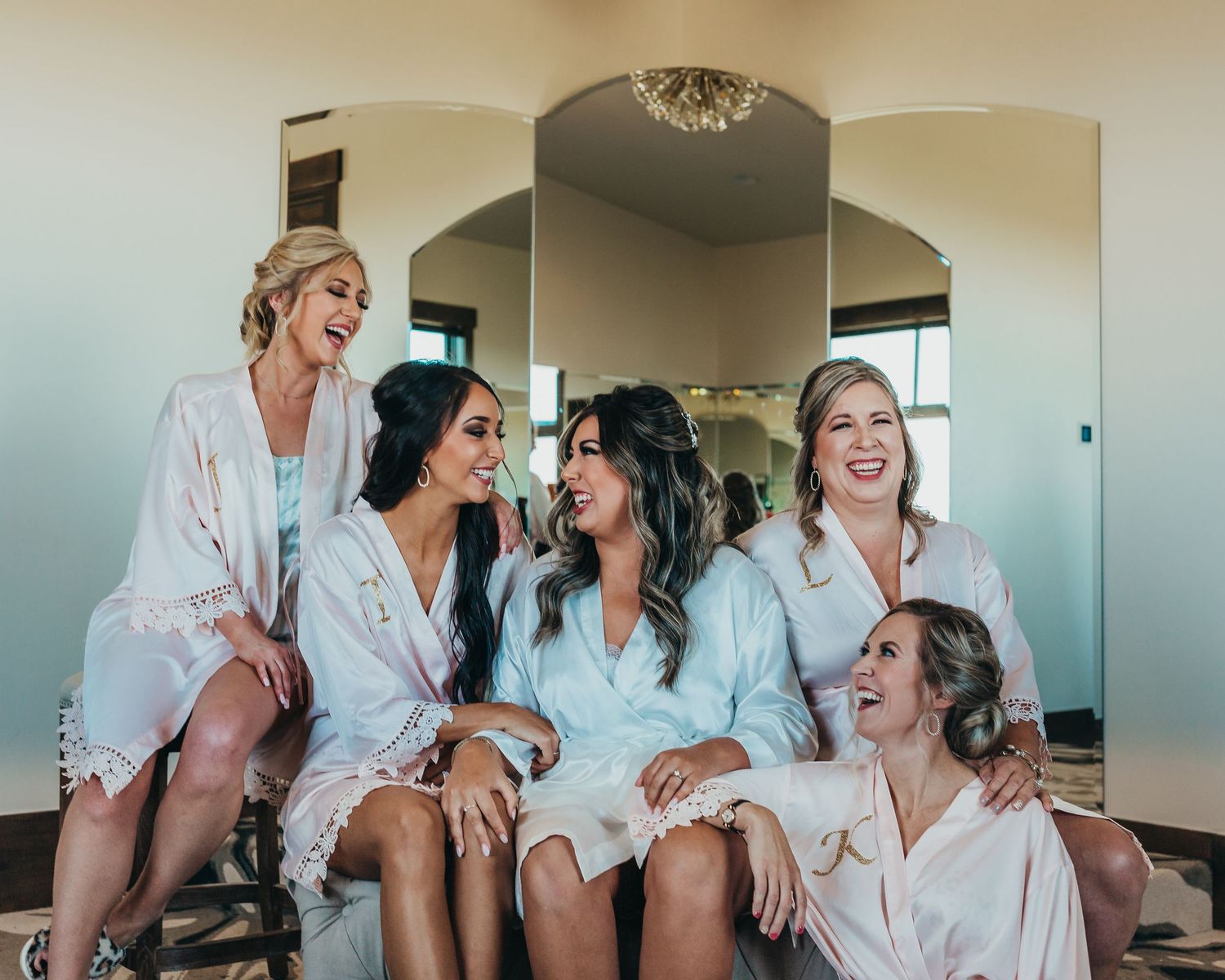 A group wearing matching white robes sits together laughing during wedding preparations.