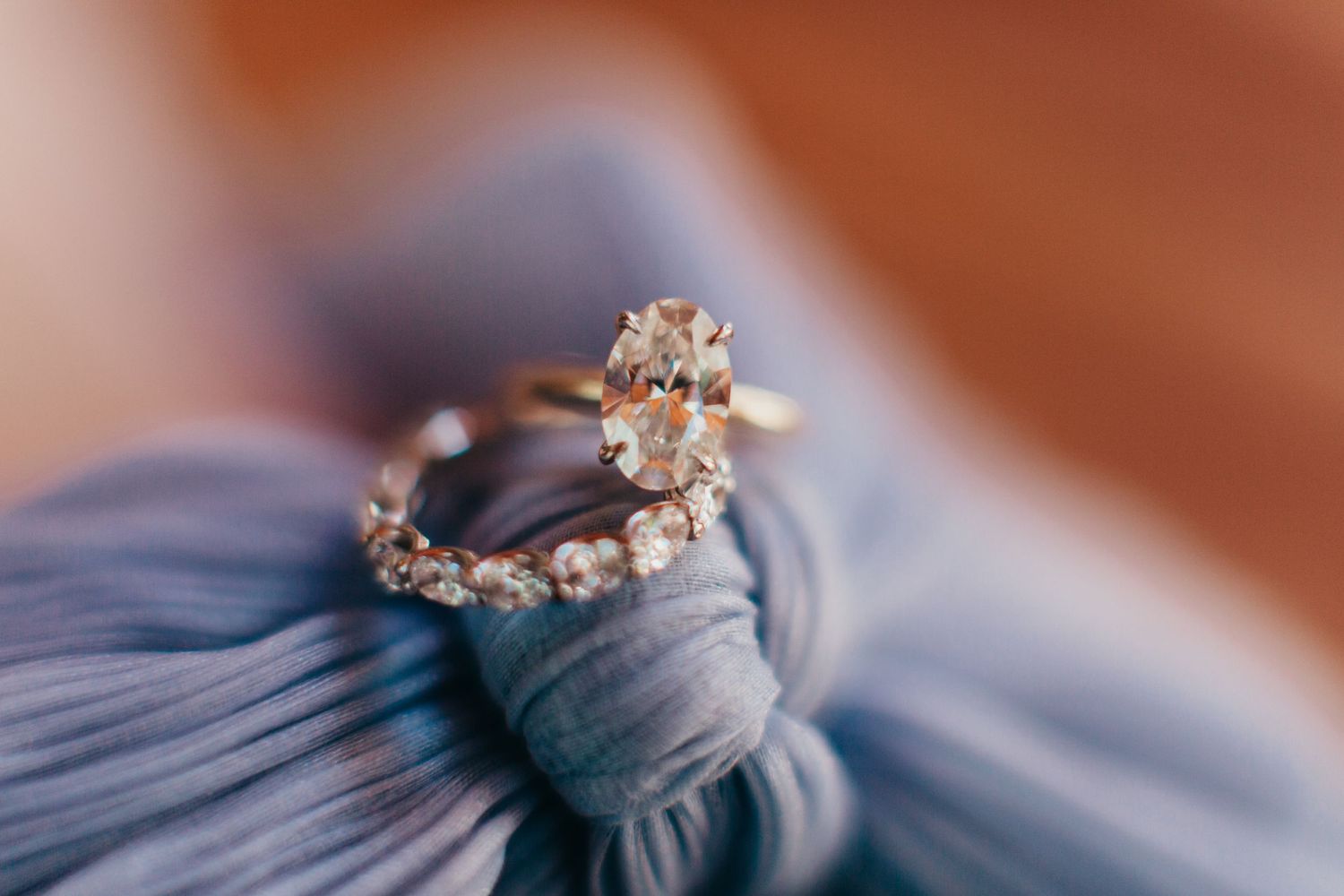 Sparkling diamond engagement ring and wedding band displayed on blue fabric.