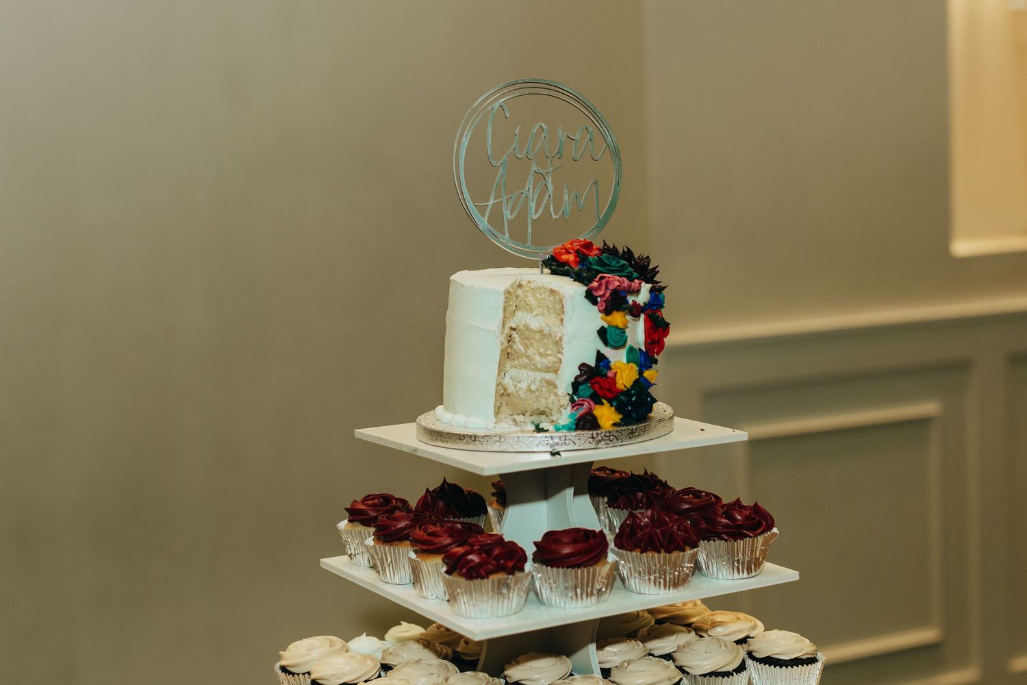 Tiered wedding cake display with colorful decorations and cupcakes.