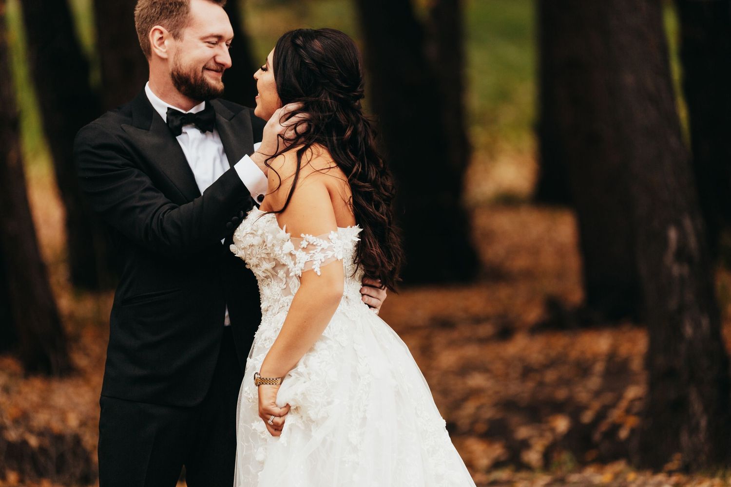 A romantic moment between newlyweds sharing laughter in a forest setting.