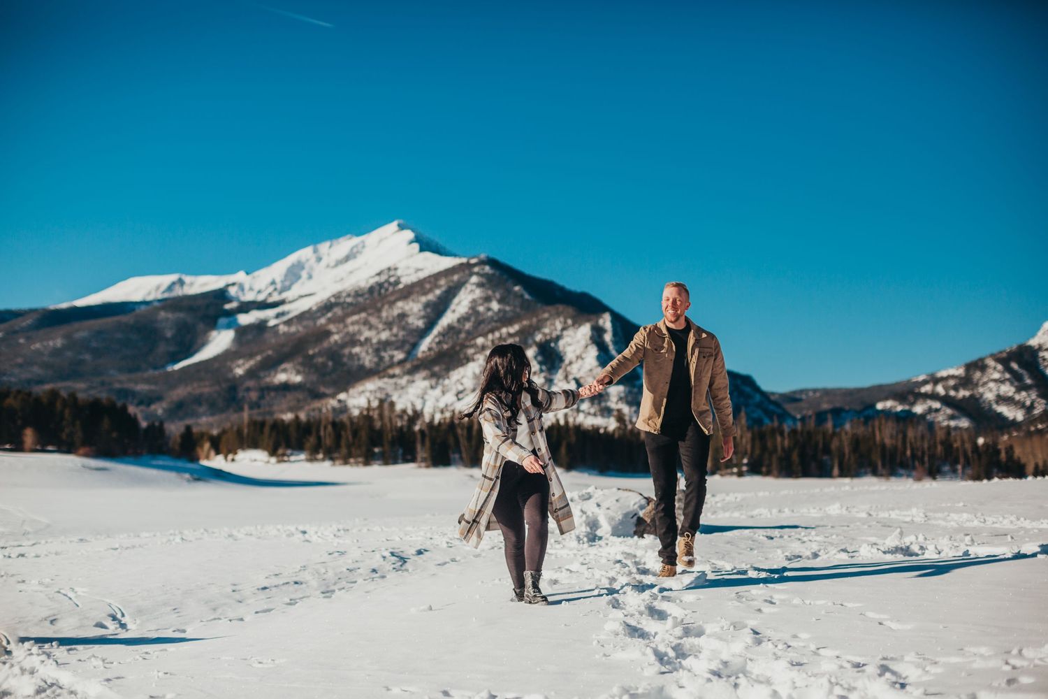 Two people walking hand in hand through snowy mountains on a clear winter day.